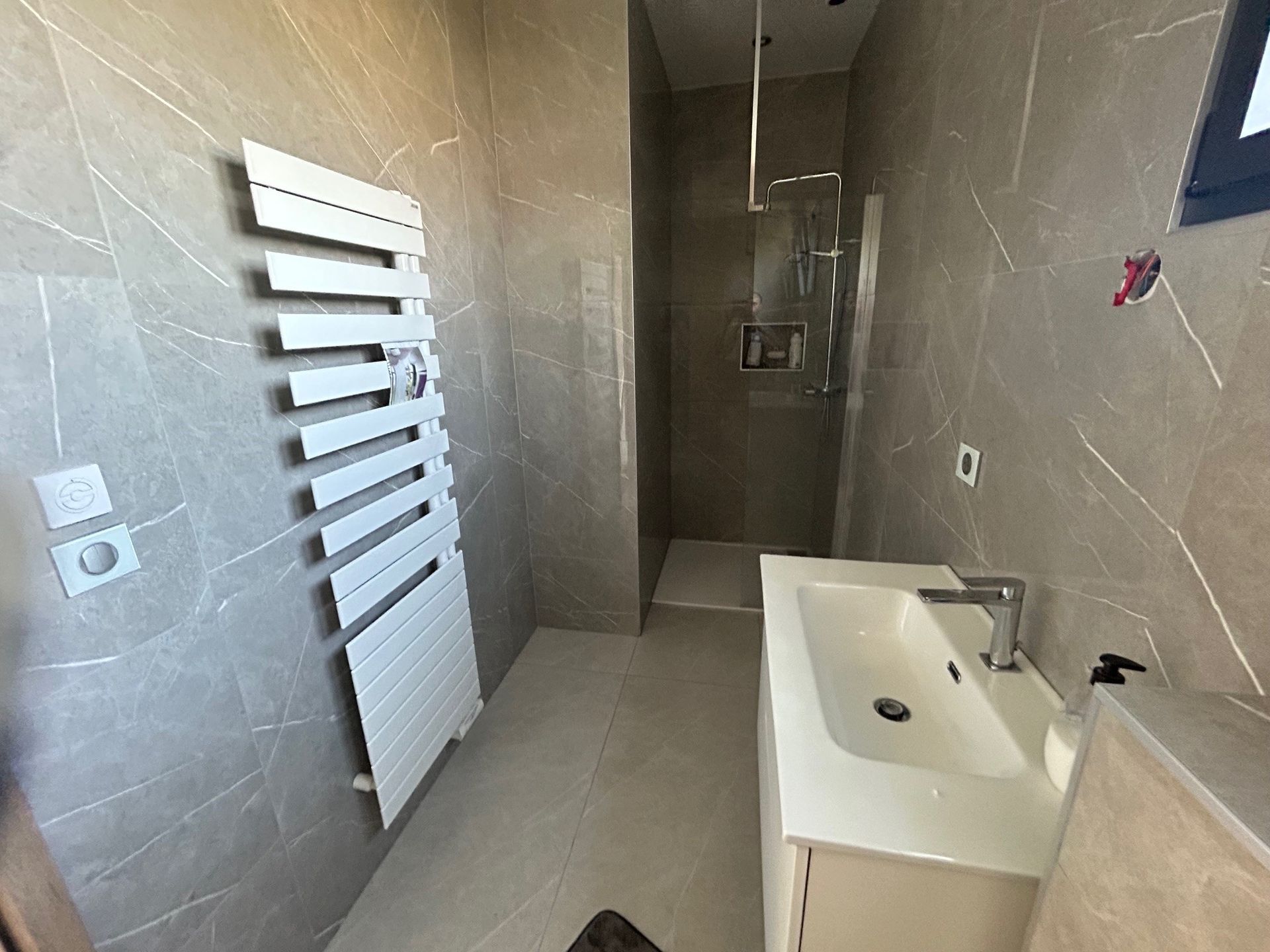 Salle de bains moderne avec murs carrelés gris, lavabo blanc, sèche-serviettes et douche à l'italienne.