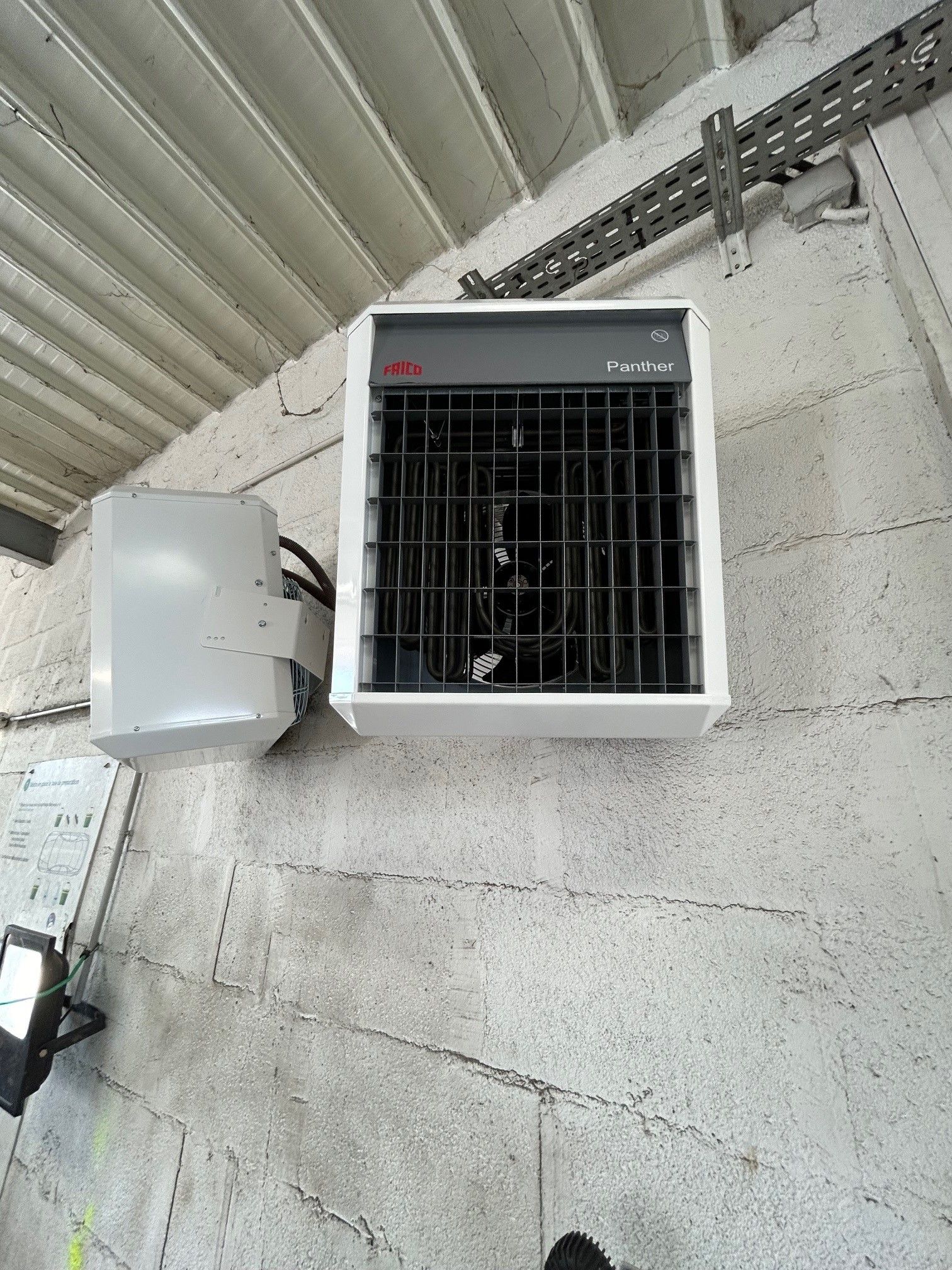 Chauffage électrique mural gris et boîtier de commande dans un bâtiment en béton.