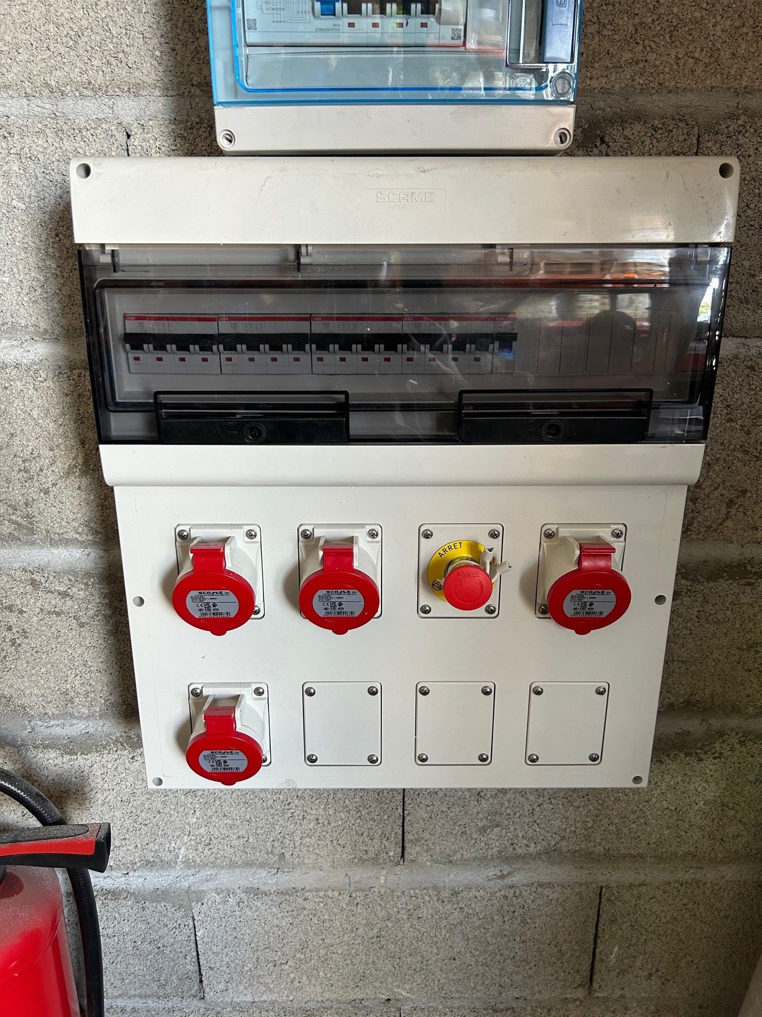 Tableau électrique avec prises de courant rouges et bouton d'arrêt d'urgence sur un mur en briques.