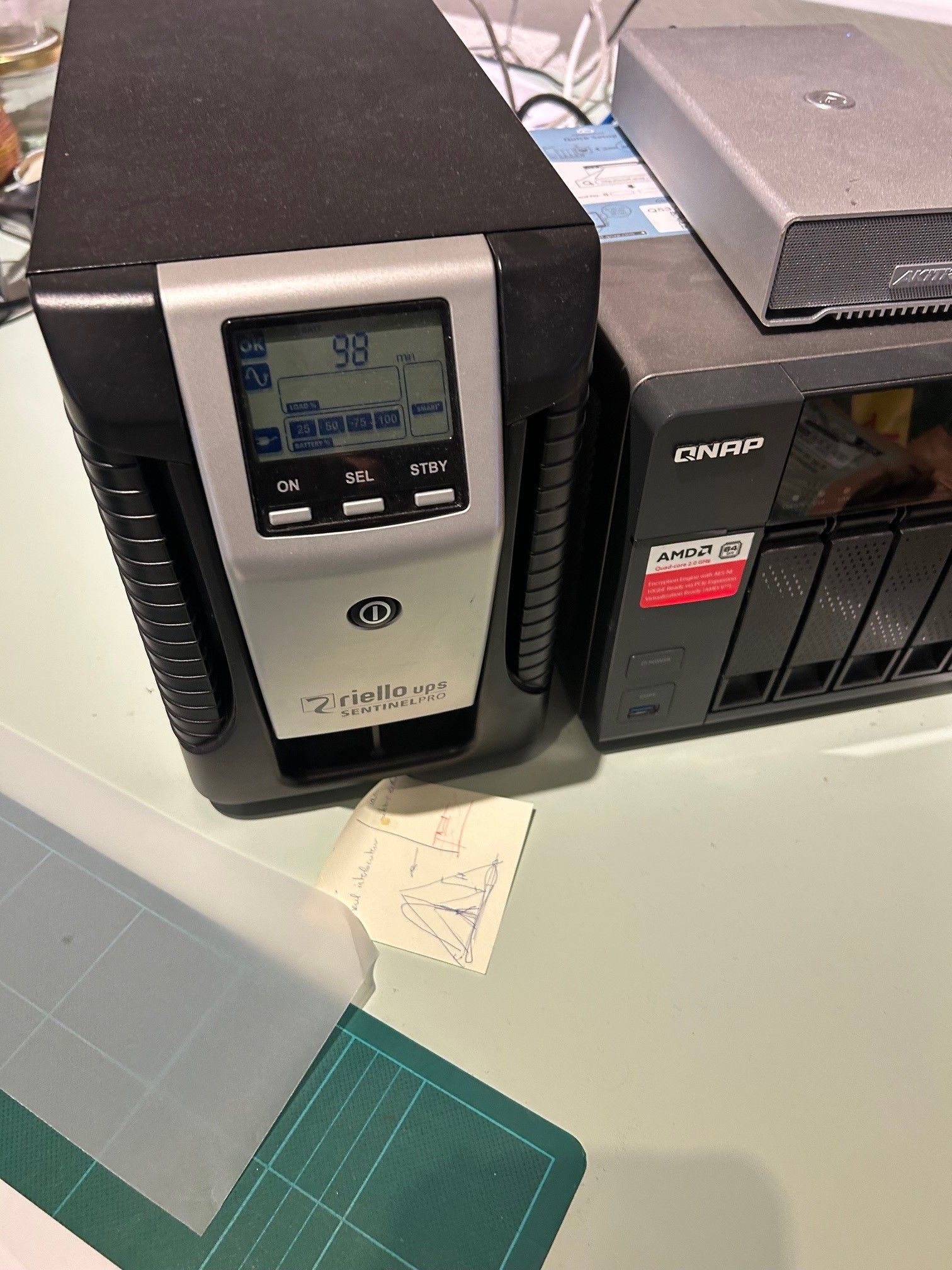 Onduleur (Intellipower) et NAS QNAP sur une table. L'écran affiche 98 % de charge.