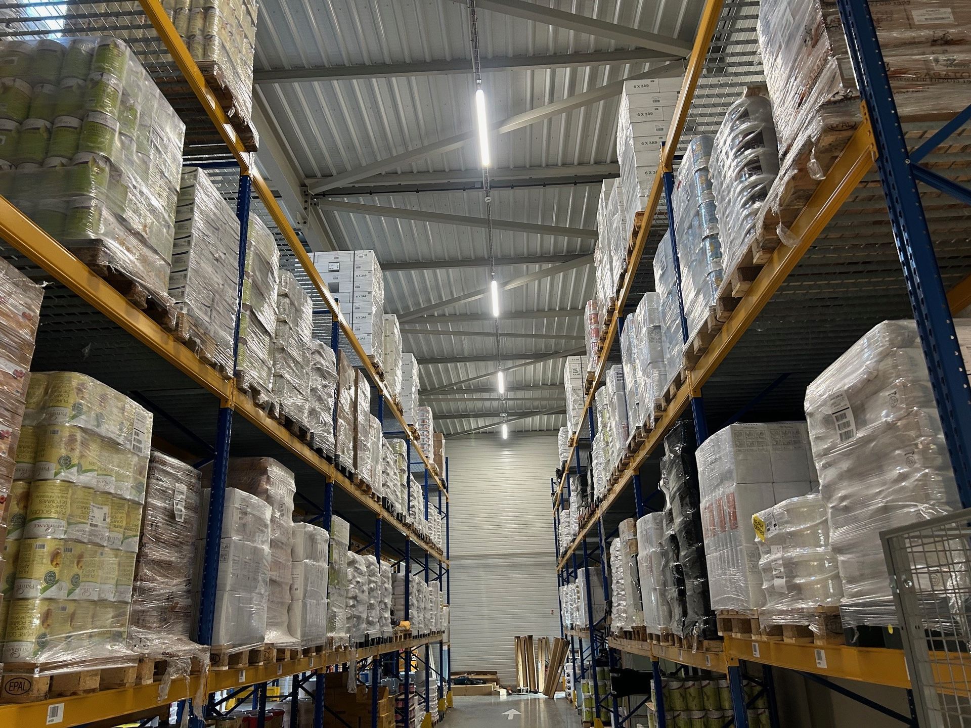 Intérieur d'un entrepôt avec des palettes de marchandises emballées empilées sur des étagères métalliques.