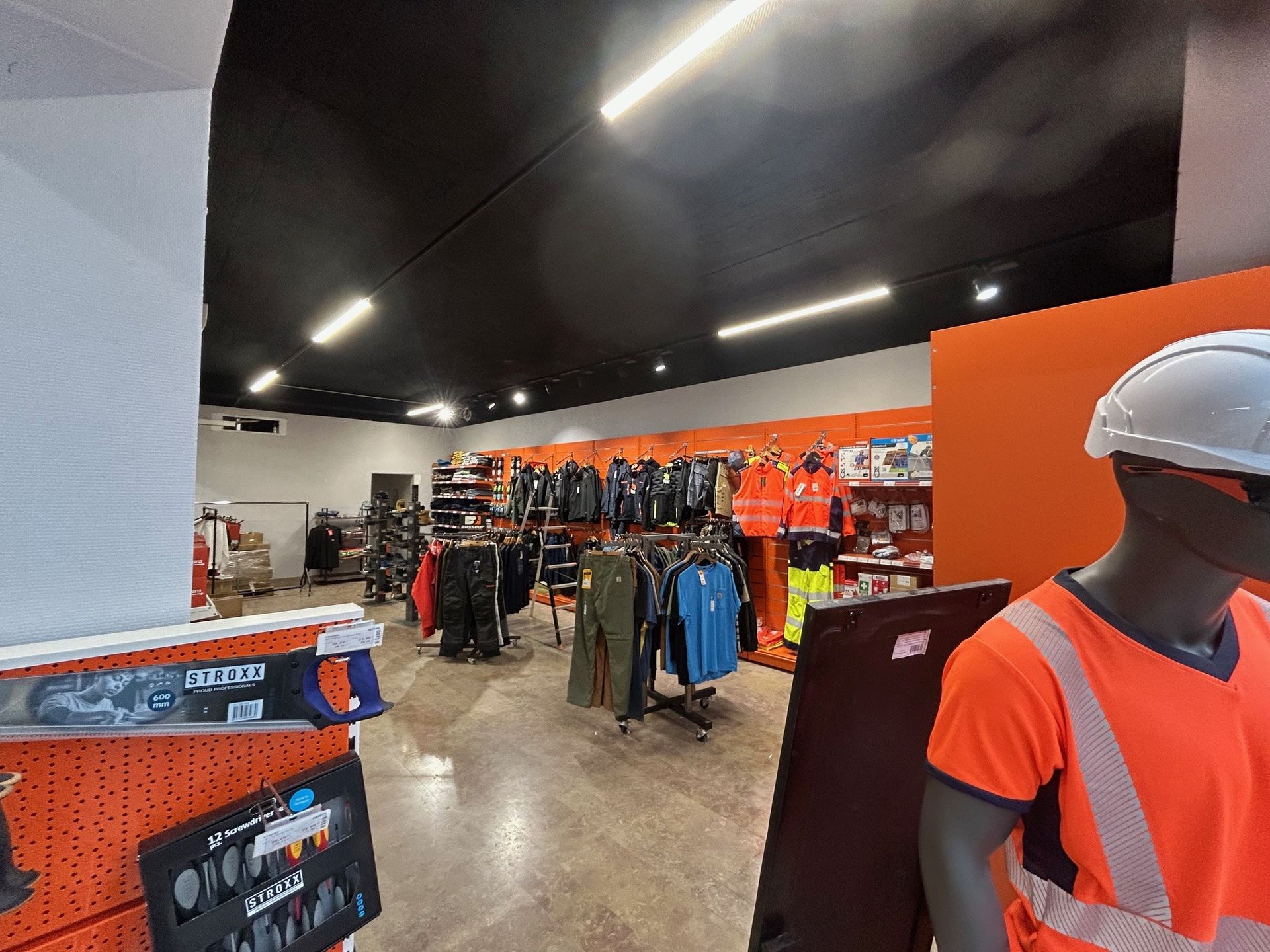 À l'intérieur d'un magasin de vêtements de travail. On aperçoit des présentoirs de vêtements et d'équipements de sécurité.