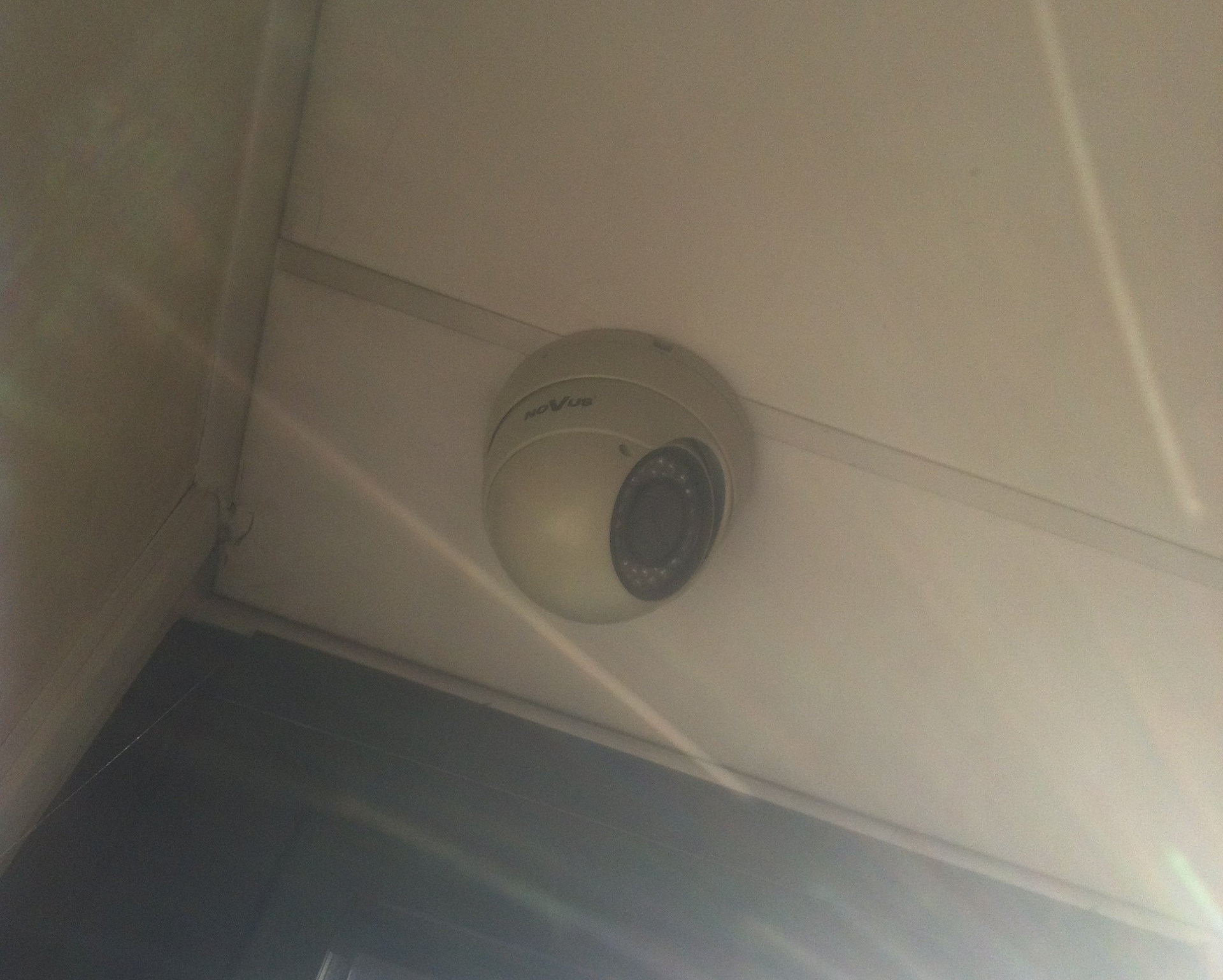 Caméra de sécurité fixée au plafond blanc, inclinée vers le bas.