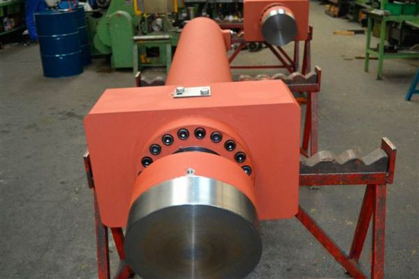 Un gran cilindro naranja está sobre un soporte rojo.