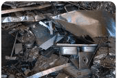 Un objeto metálico aplastado entre papel de aluminio plateado retorcido y escombros, que recuerda a restos industriales o chatarra.