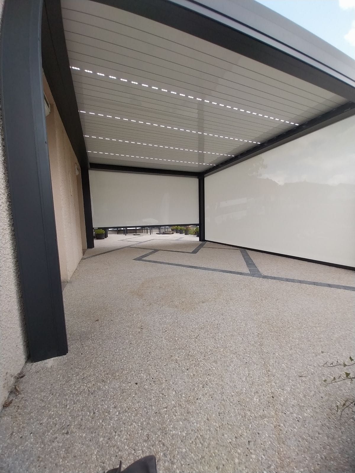 Panneaux coulissants déployés autour d'un carport sur une dalle de béton.