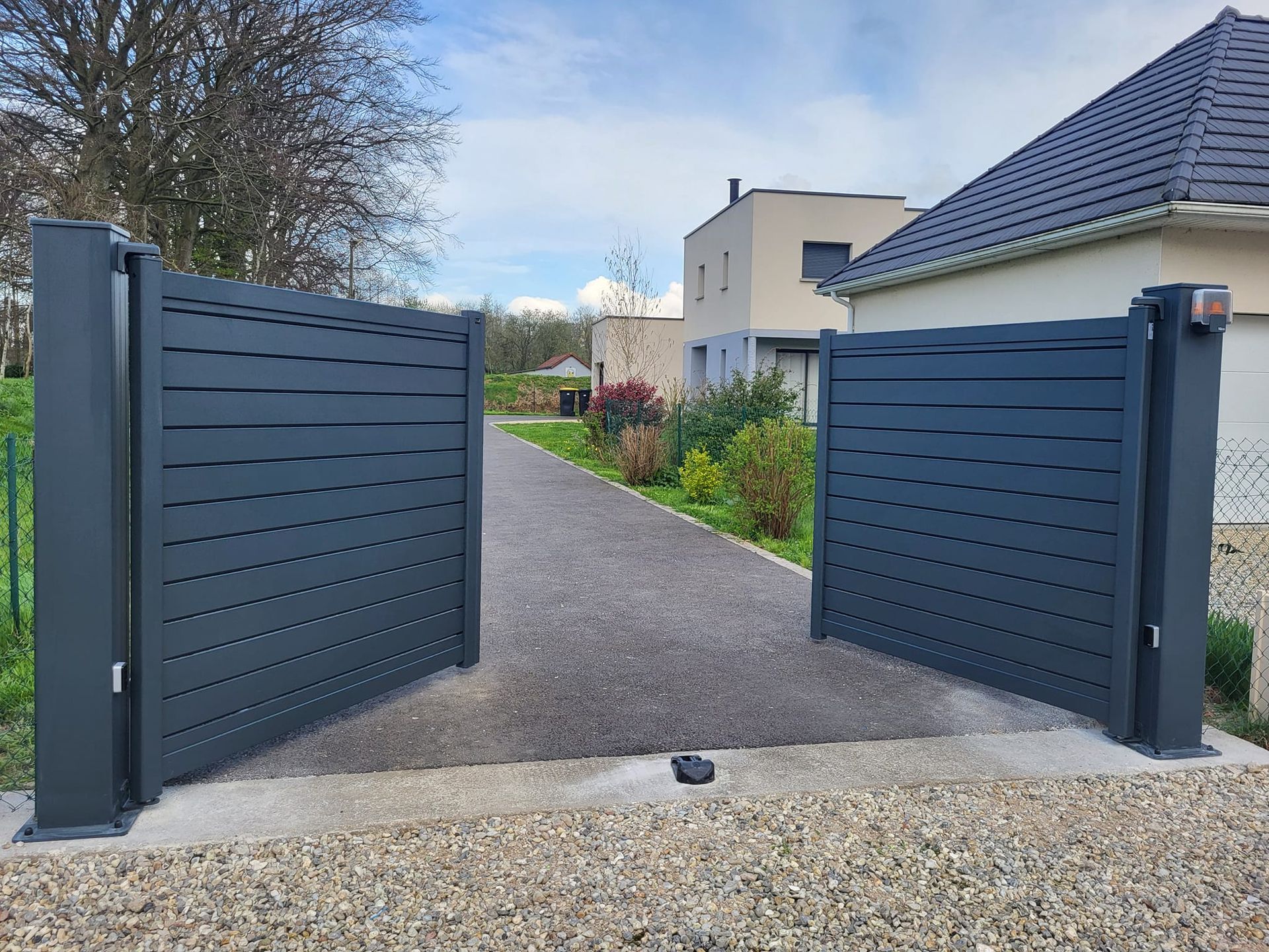 Portail noir anthracite à moitié ouvert donnant sur des lotissements.