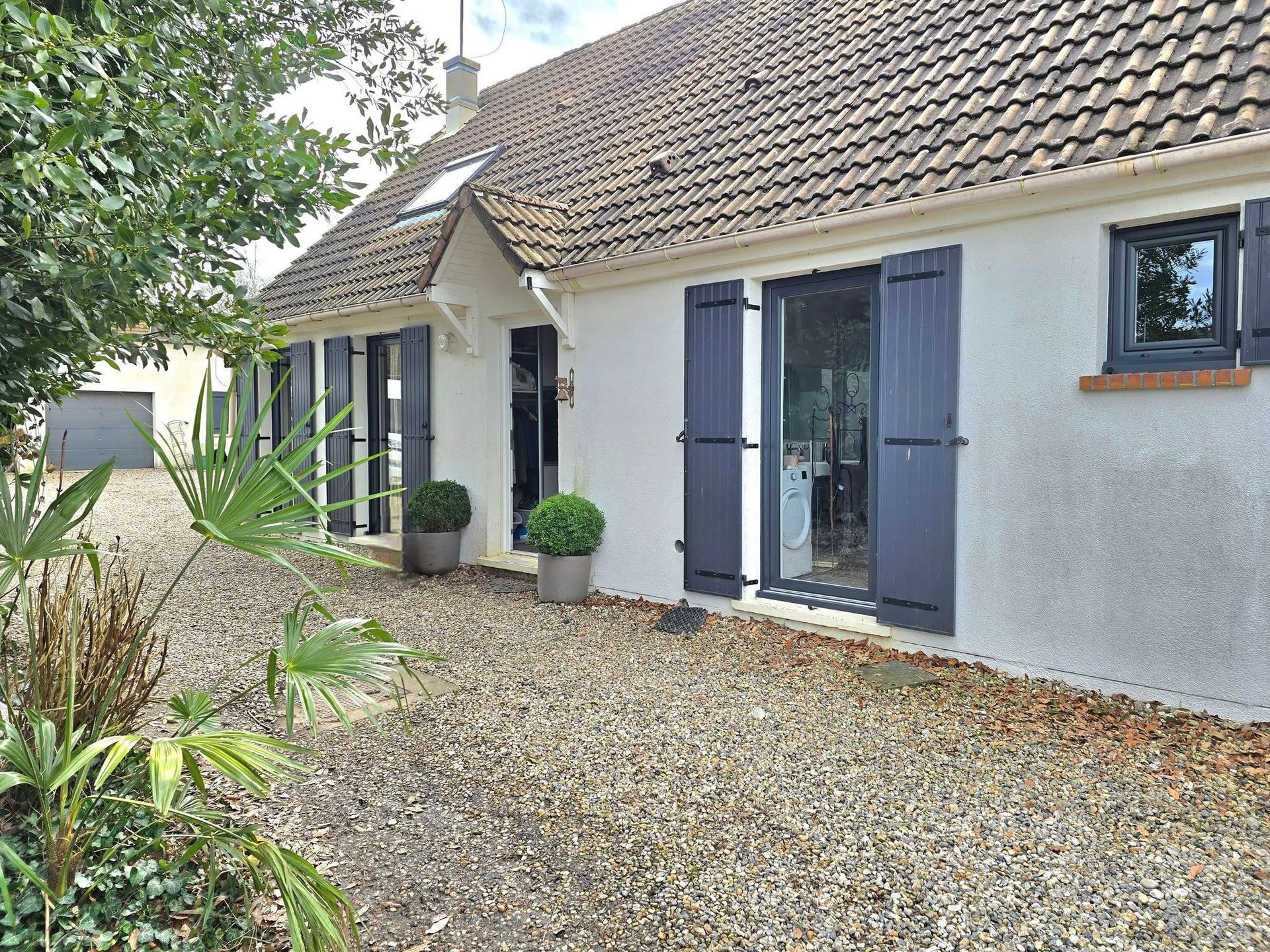 Maison de plain-pied sur un terrain recouvert de cailloux avec au loin un garage.