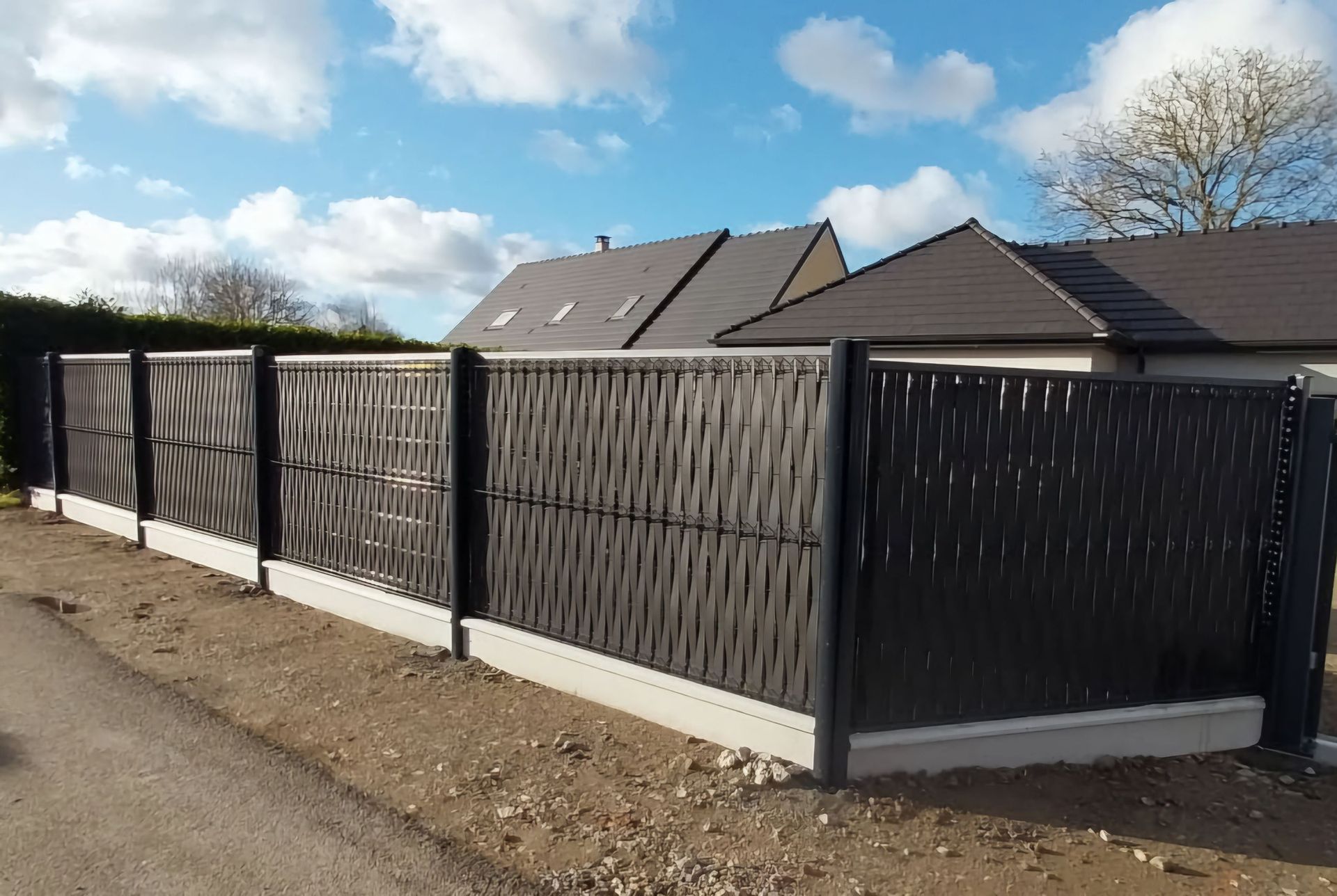Clôture occultante noire posée sur un petit muret autour d'une propriété.
