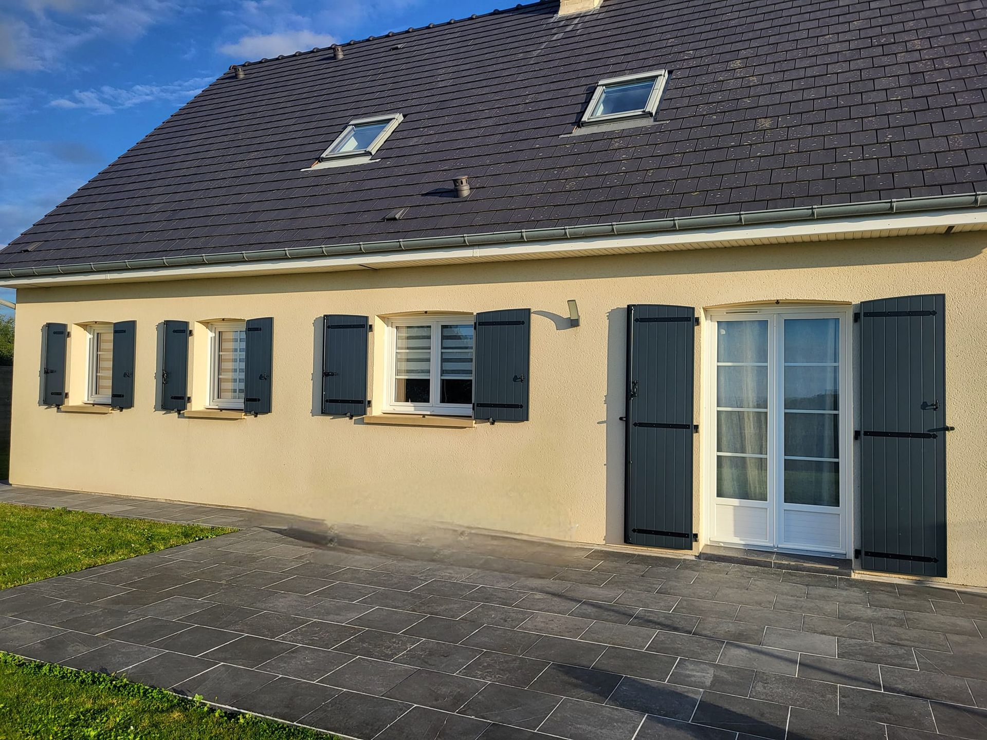 Maison de plain-pied aux volets noirs ouverts.