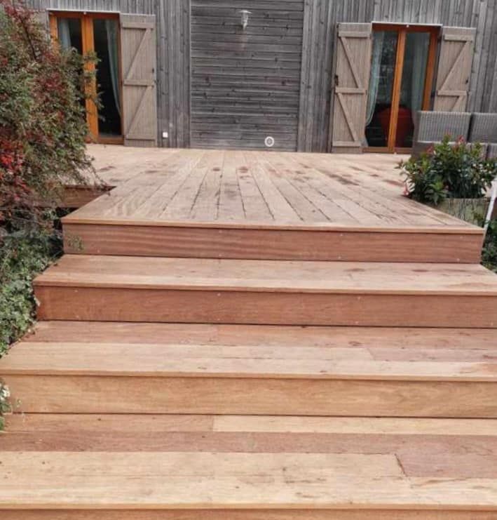 Gros plan sur des escaliers en bois menant vers une terrasse en bois.