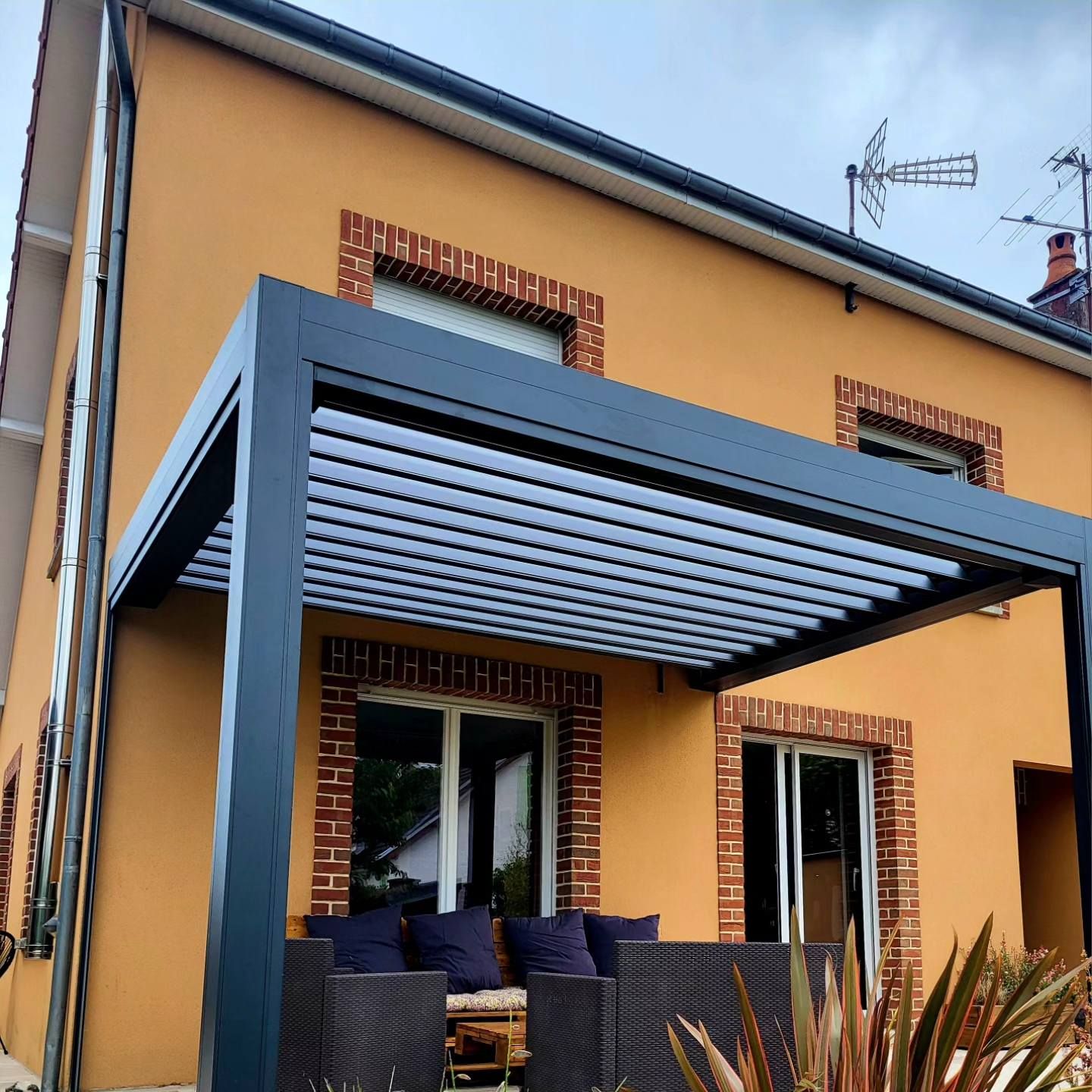 Pergola contre une habitation à la façade jaune.