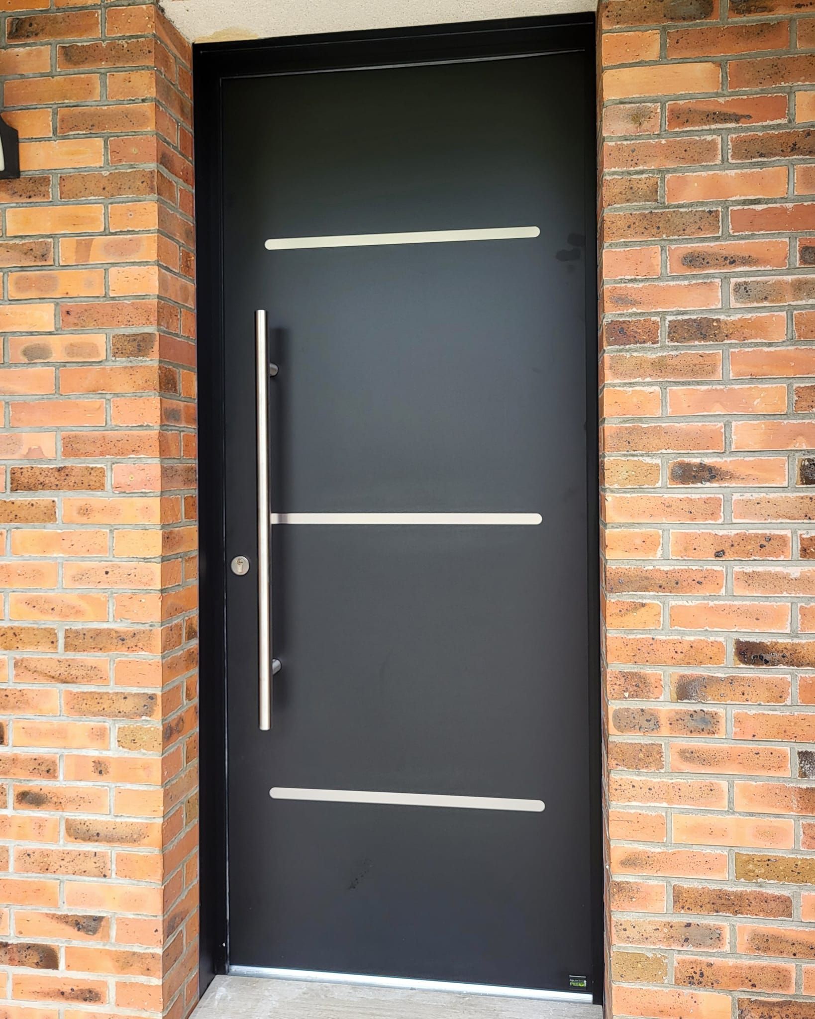 Porte d'entrée en aluminium encastrée dans un mur en briques.