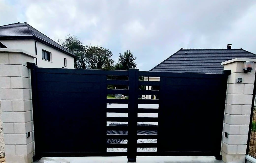 Portail noir entre deux piliers de briques blanches.