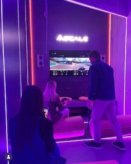 Un hombre y una mujer están jugando un videojuego en una habitación con luces violetas.