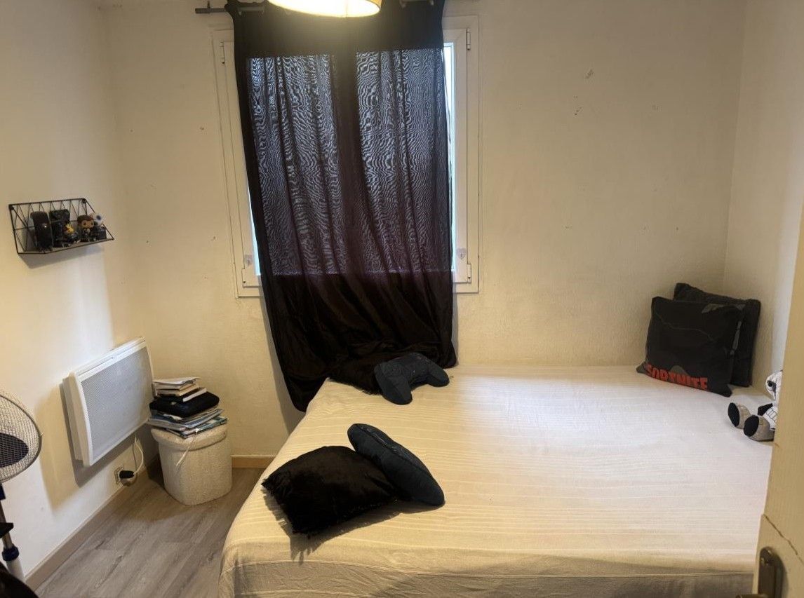 Chambre avec lit blanc, rideaux noirs à la fenêtre et radiateur mural