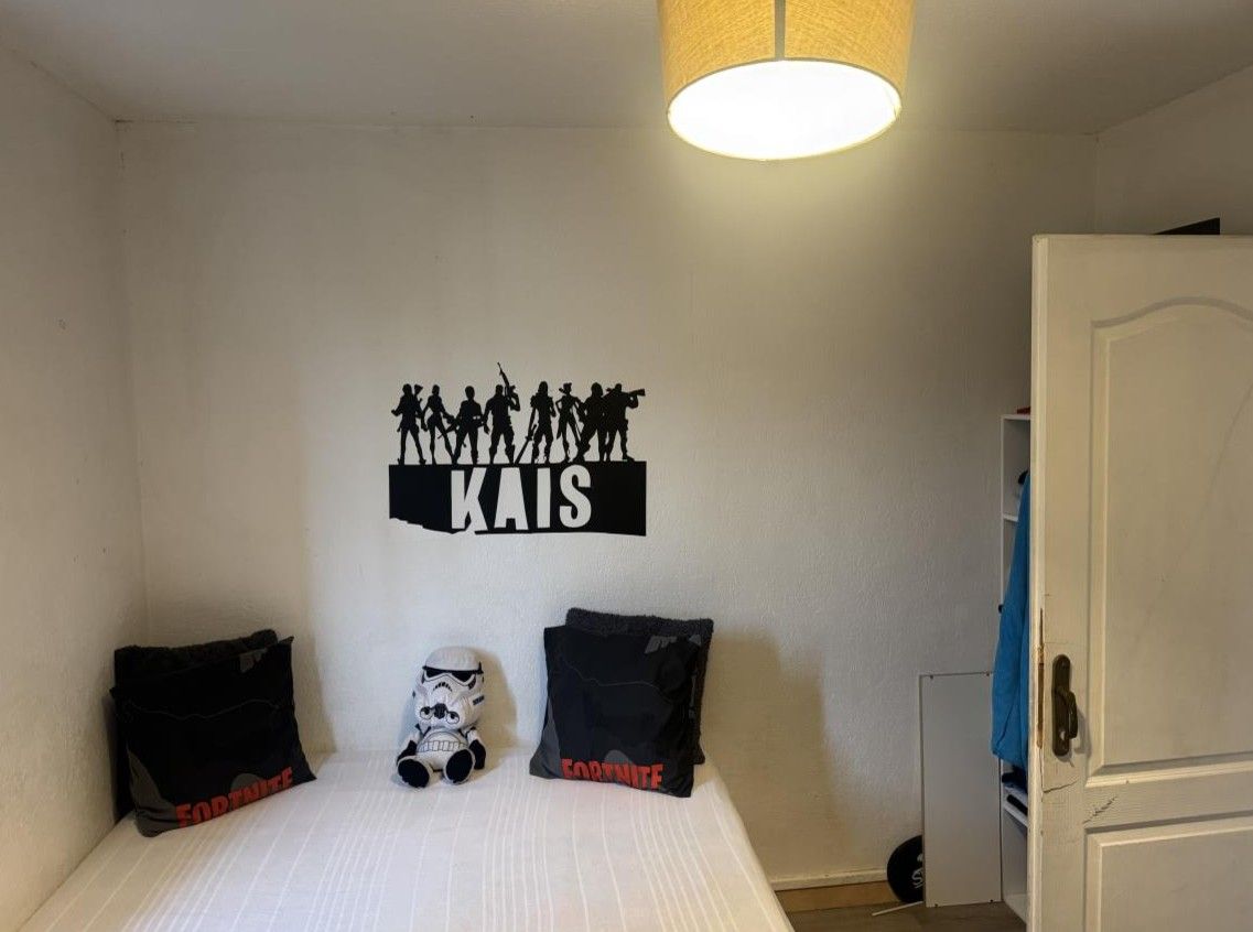 Chambre rangée avec lit blanc, peluche Stormtrooper et lettres du prénom KAIS au mur
