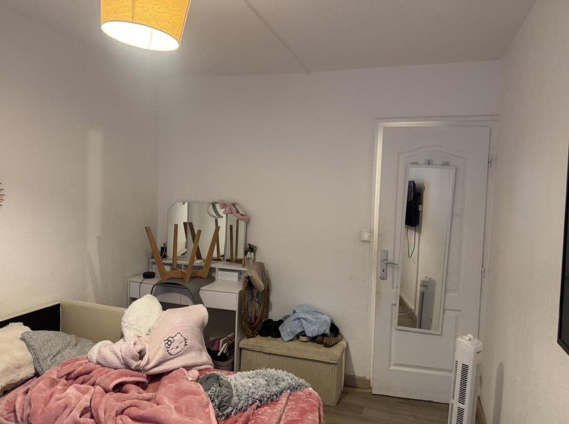 Chambre désordonnée avec couvertures en boule sur le lit et une petite coiffeuse au fond