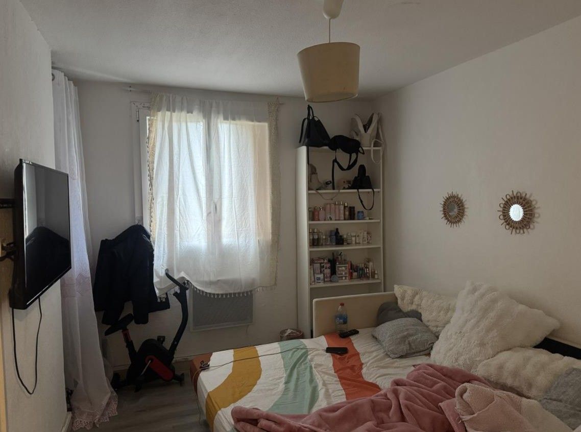 Lit avec une couette colorée ; vélo d'appartement près de la fenêtre et bibliothèque blanche au fond de la chambre