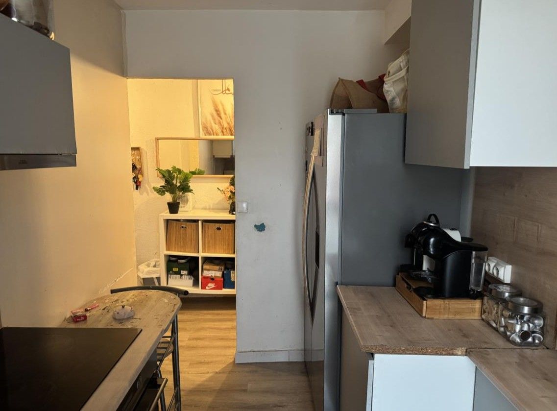 Vue sur une cuisine, avec plan de travail, réfrigérateur et machine à café