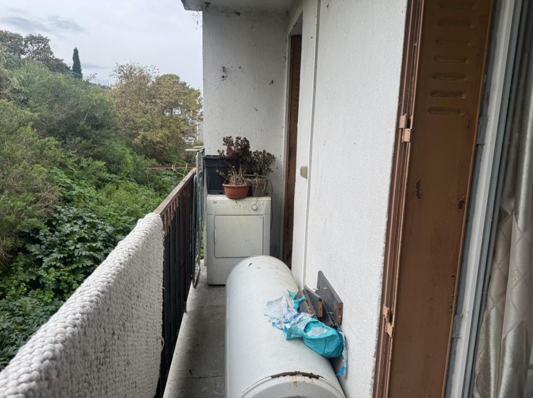 Balcon étroit avec une rambarde en bois, des plantes et une grande bonbonne blanche