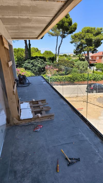 Obra: tejado plano con herramientas y materiales, rodeado de exuberante vegetación y árboles bajo un cielo azul.