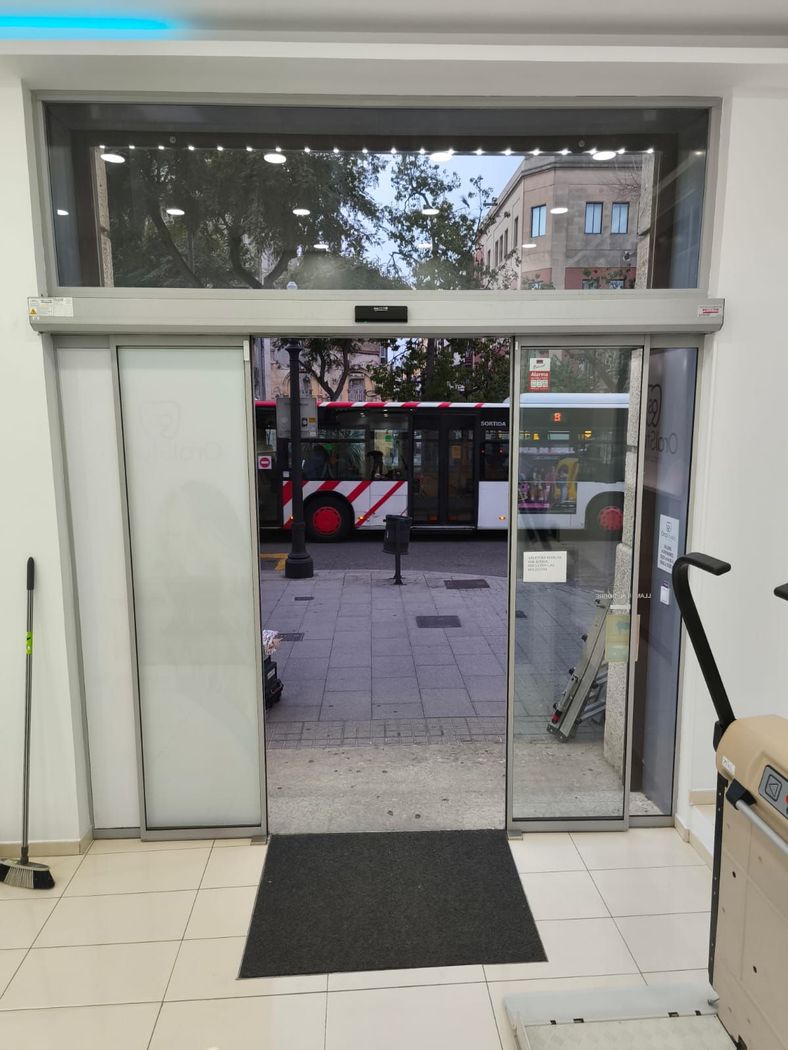 Coche deportivo gris aparcado delante de un edificio moderno con una marquesina de color azul.