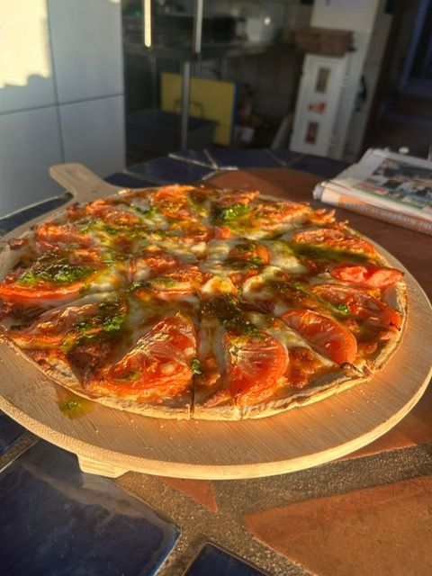 Een pizza ligt op een houten snijplank op een tafel.