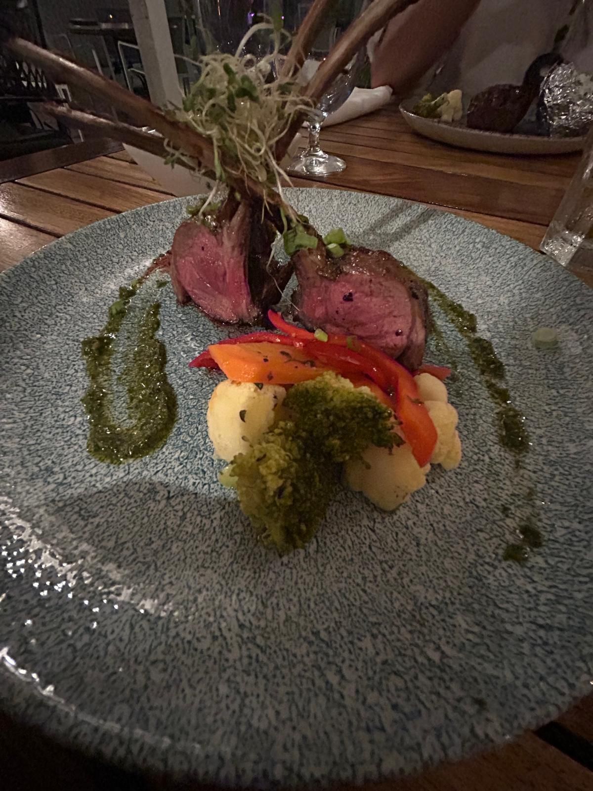 Een bord met vlees en groenten op een houten tafel.