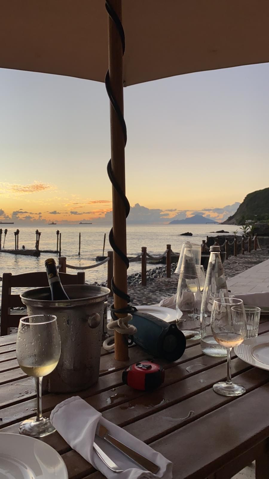 Een tafel met glazen wijn en een emmer met ijs erop, met uitzicht op de oceaan.