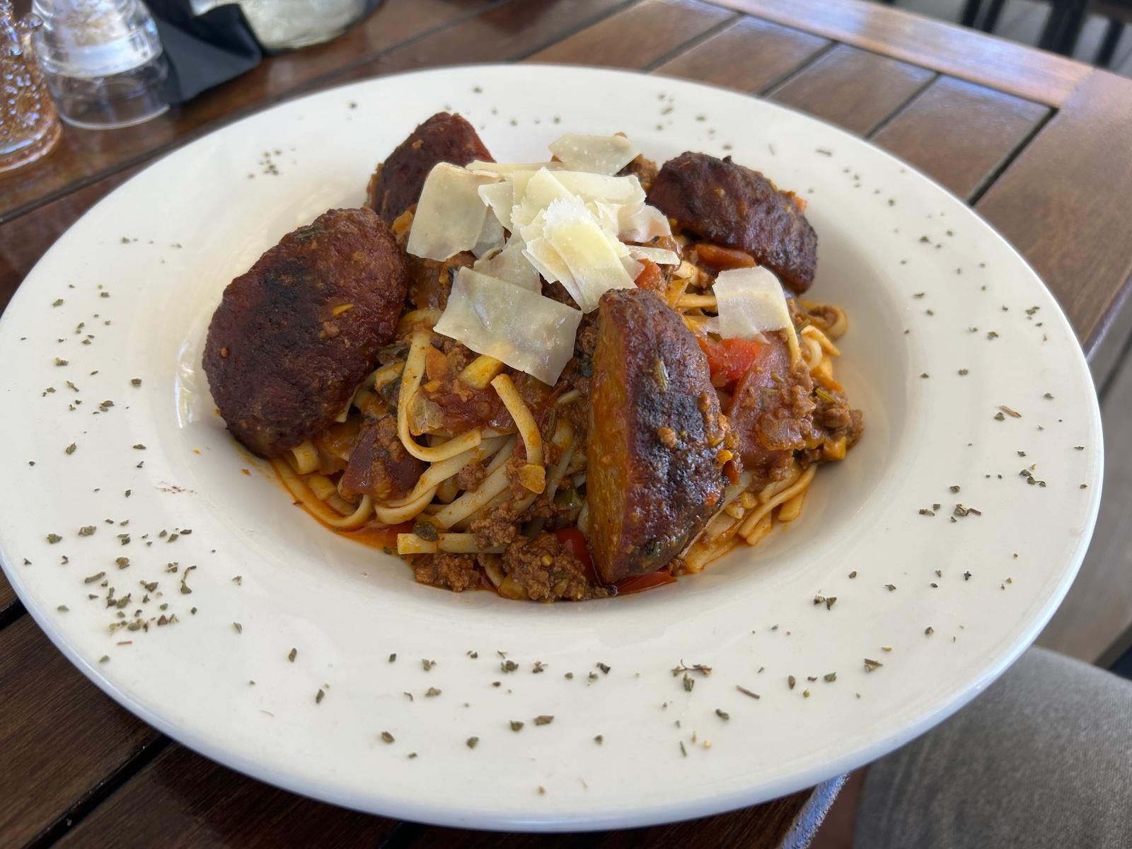 Een wit bord met spaghetti en gehaktballen op een houten tafel.