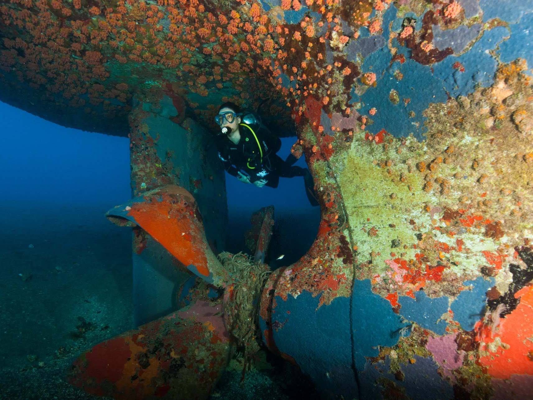 Een duiker zwemt onder een grote propeller in de oceaan.