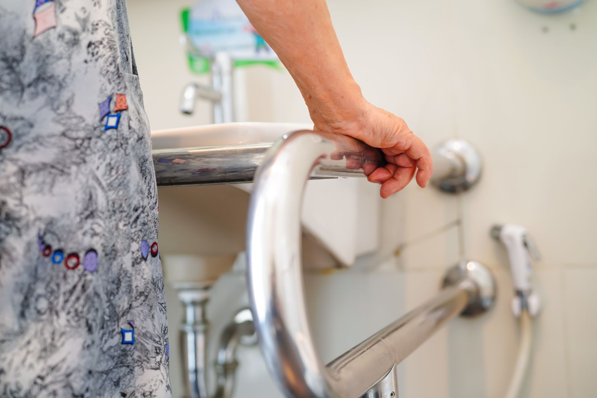 La main d'une femme saisissant une barre de sécurité chromée à côté d'un lavabo de salle de bains.