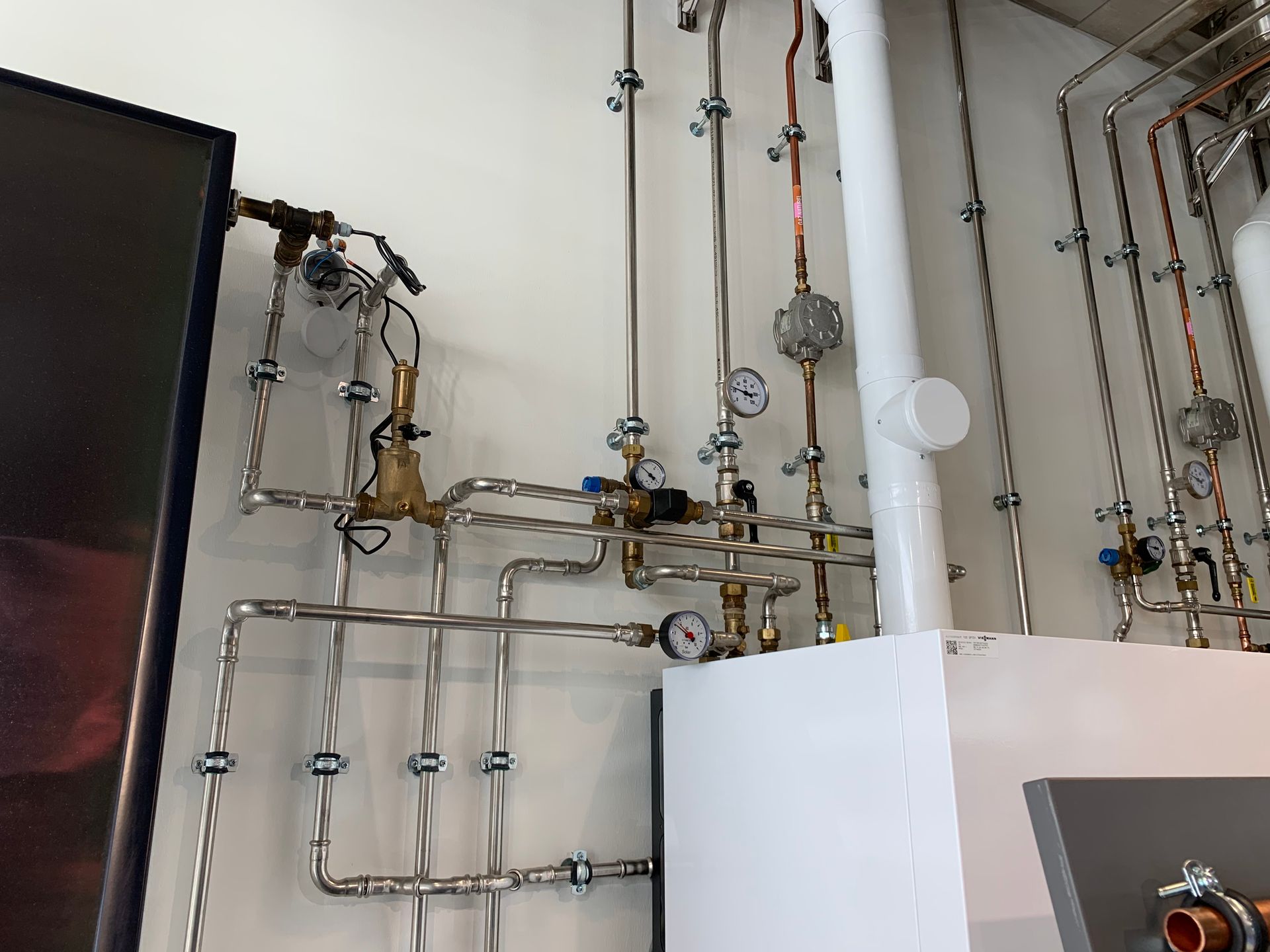 Système complexe de tuyaux, de jauges et de vannes sur un mur blanc.