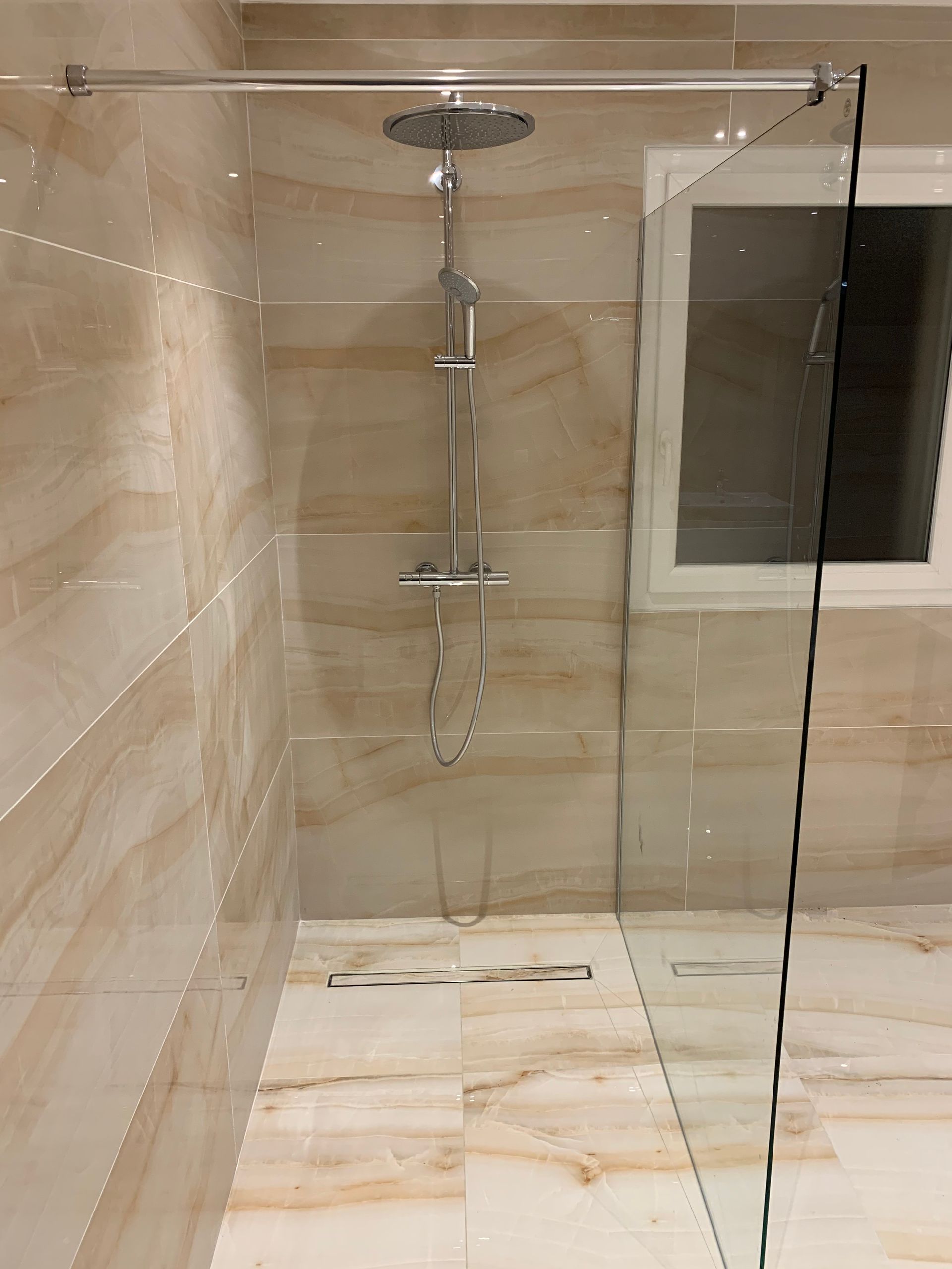 Cabine de douche en verre avec accessoires chromés dans une salle de bains carrelée beige.
