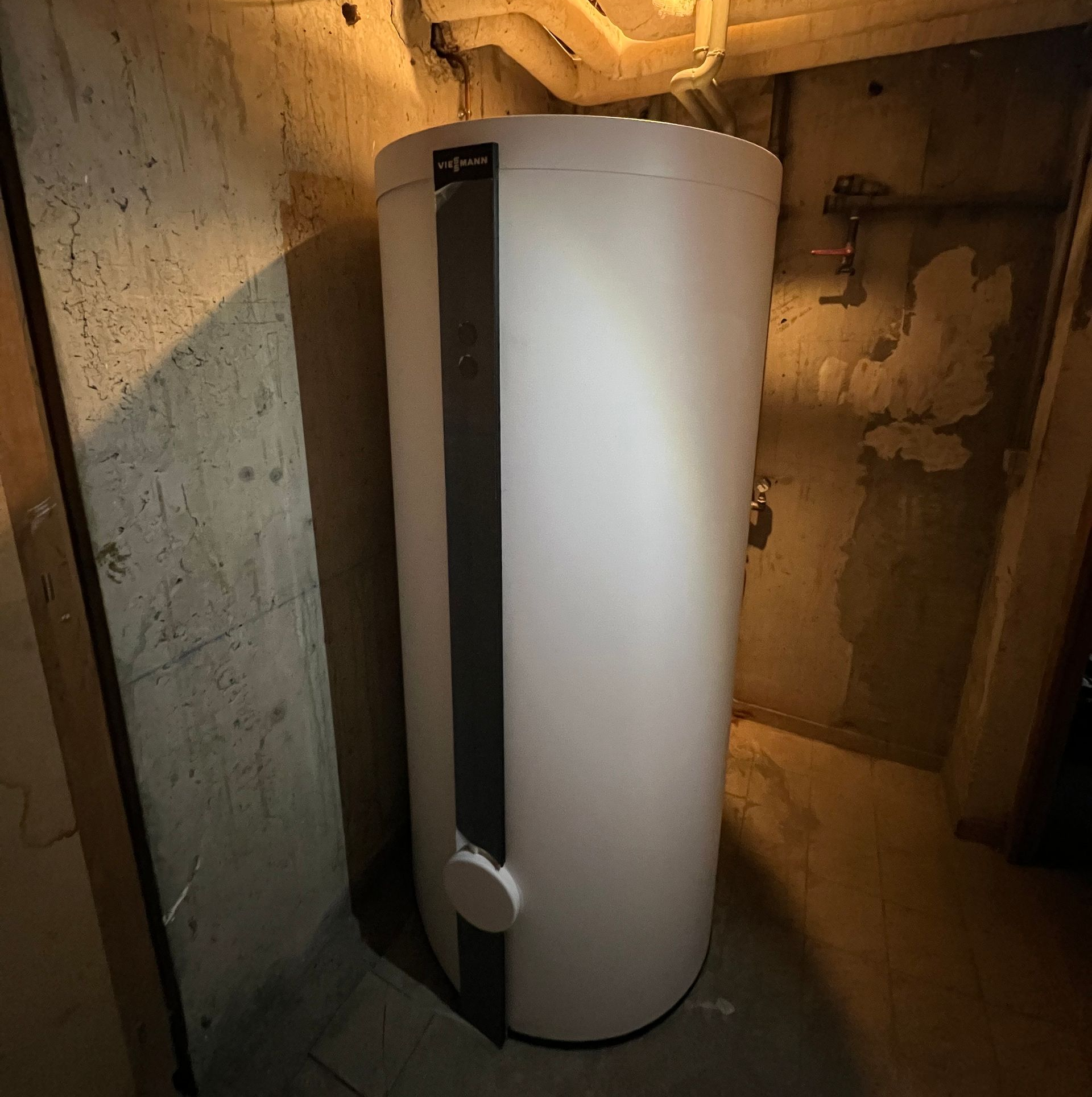 Chauffe-eau blanc de grande taille dans un sous-sol en béton.
