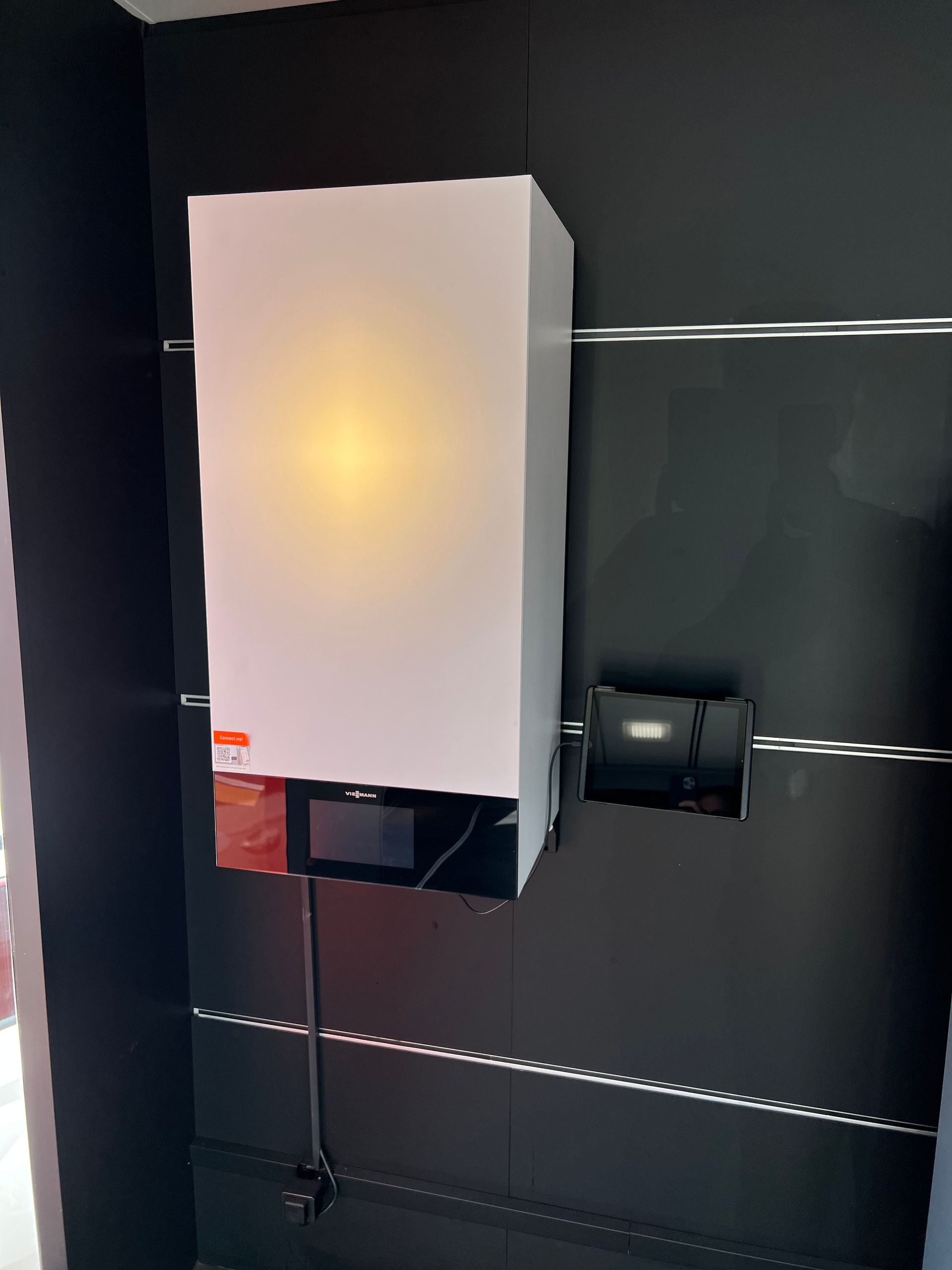 Onduleur solaire rectangulaire blanc monté sur un mur noir, connecté à un boîtier noir plus petit.