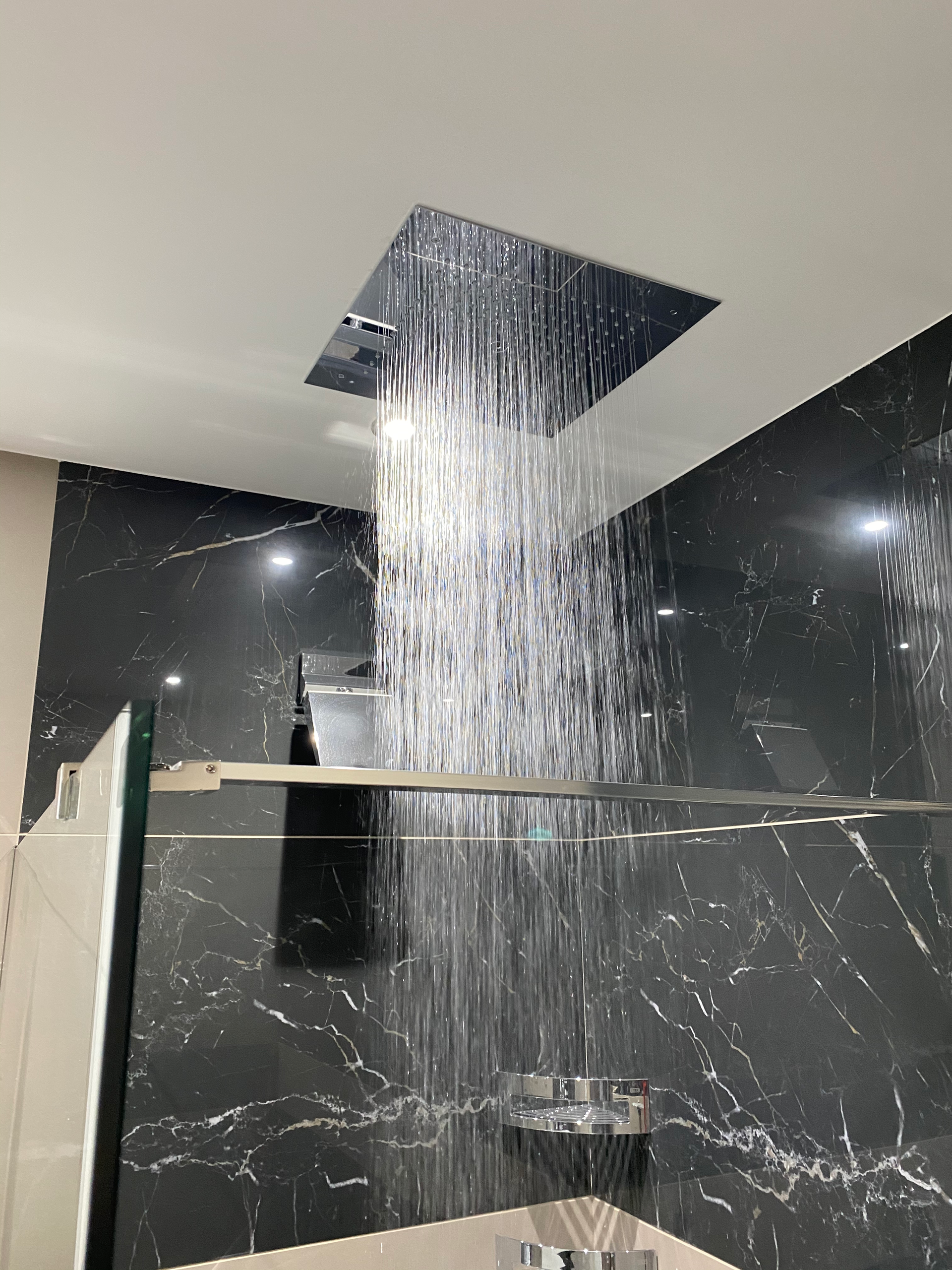 Pommeau de douche pulvérisant de l'eau dans une salle de bain moderne avec des murs en marbre noir.