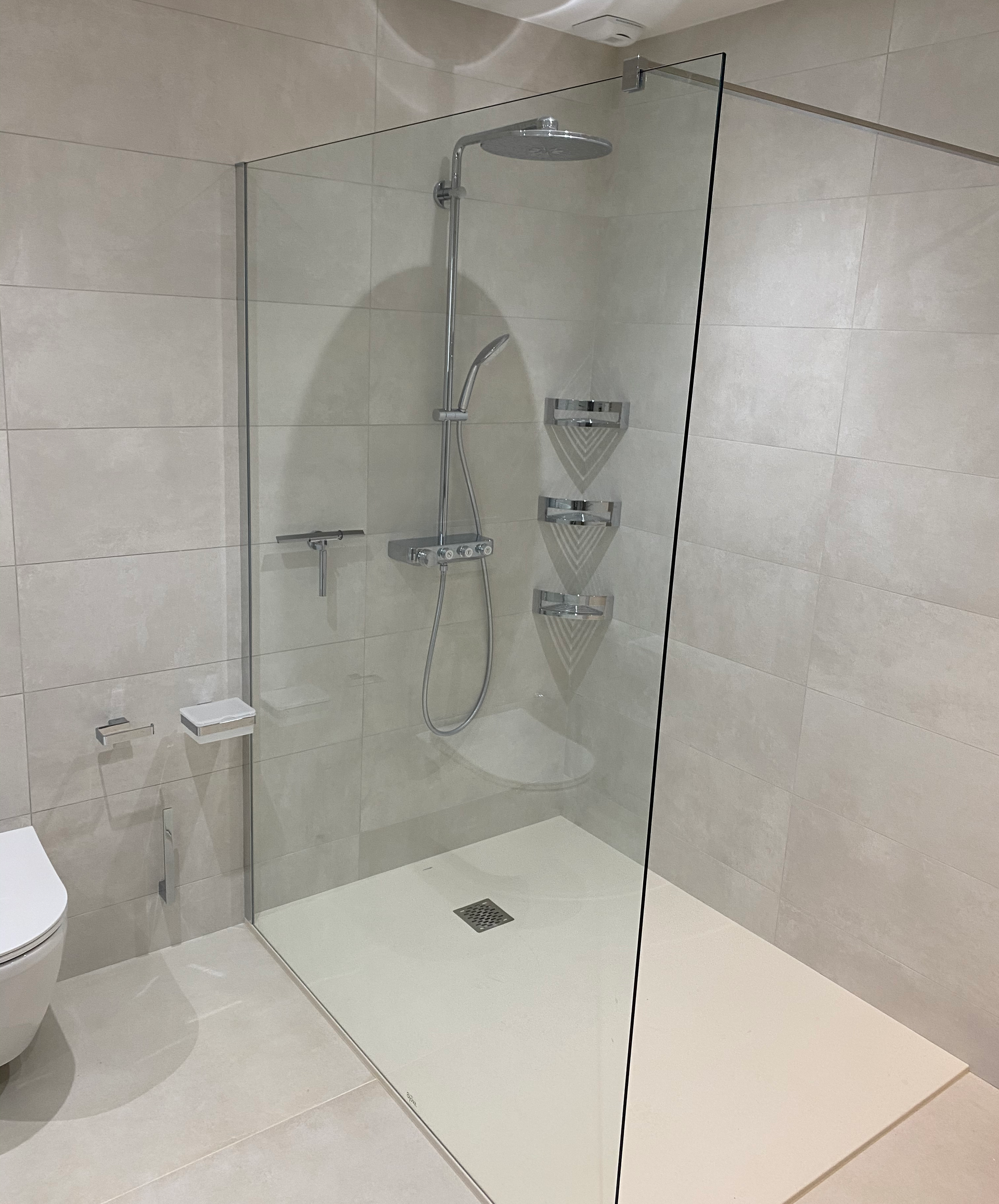 Cabine de douche moderne avec parois en verre, carrelage blanc, accessoires de douche et base de douche blanche.