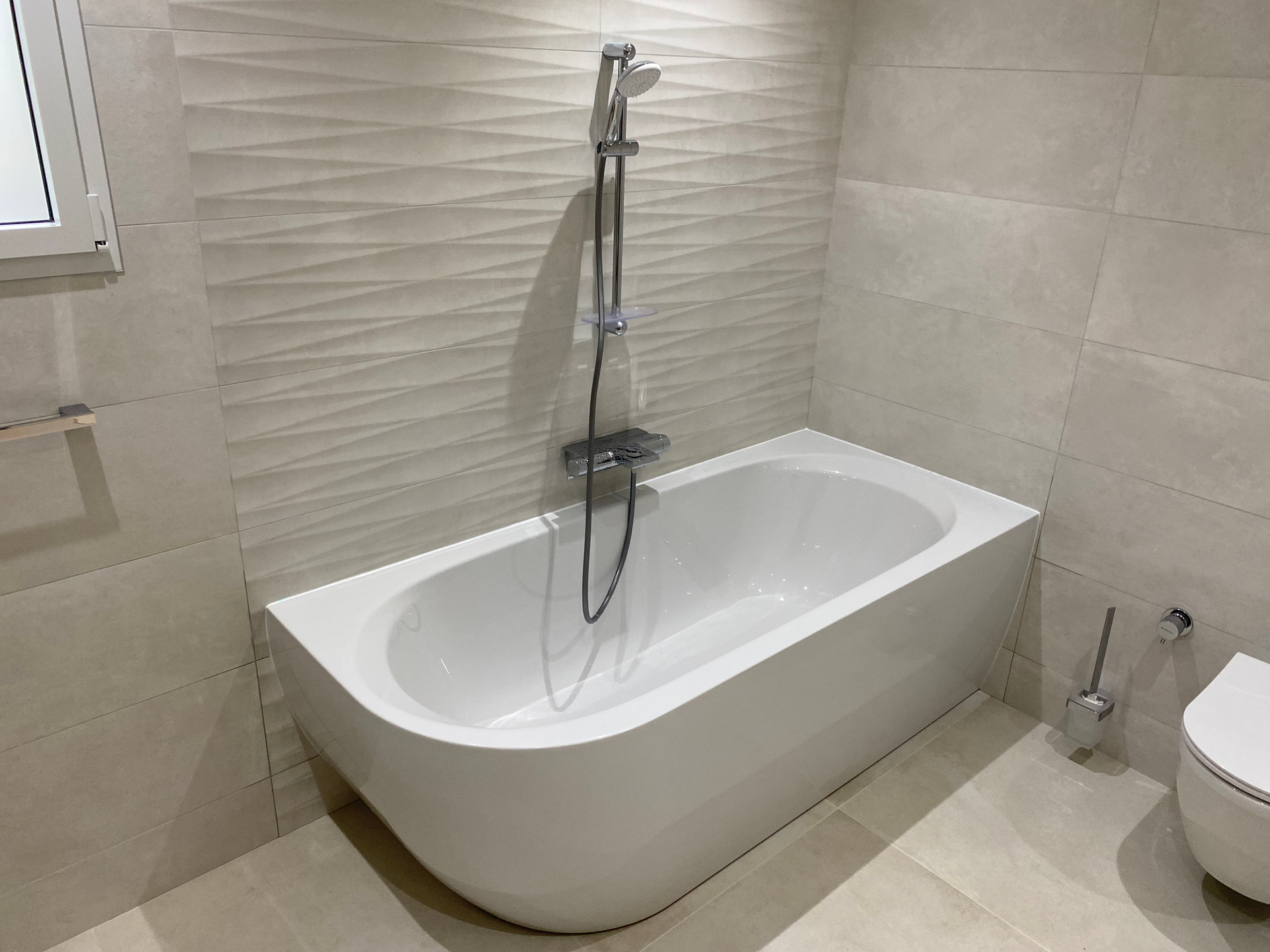 Baignoire blanche avec pommeau de douche et toilettes dans une salle de bains moderne.