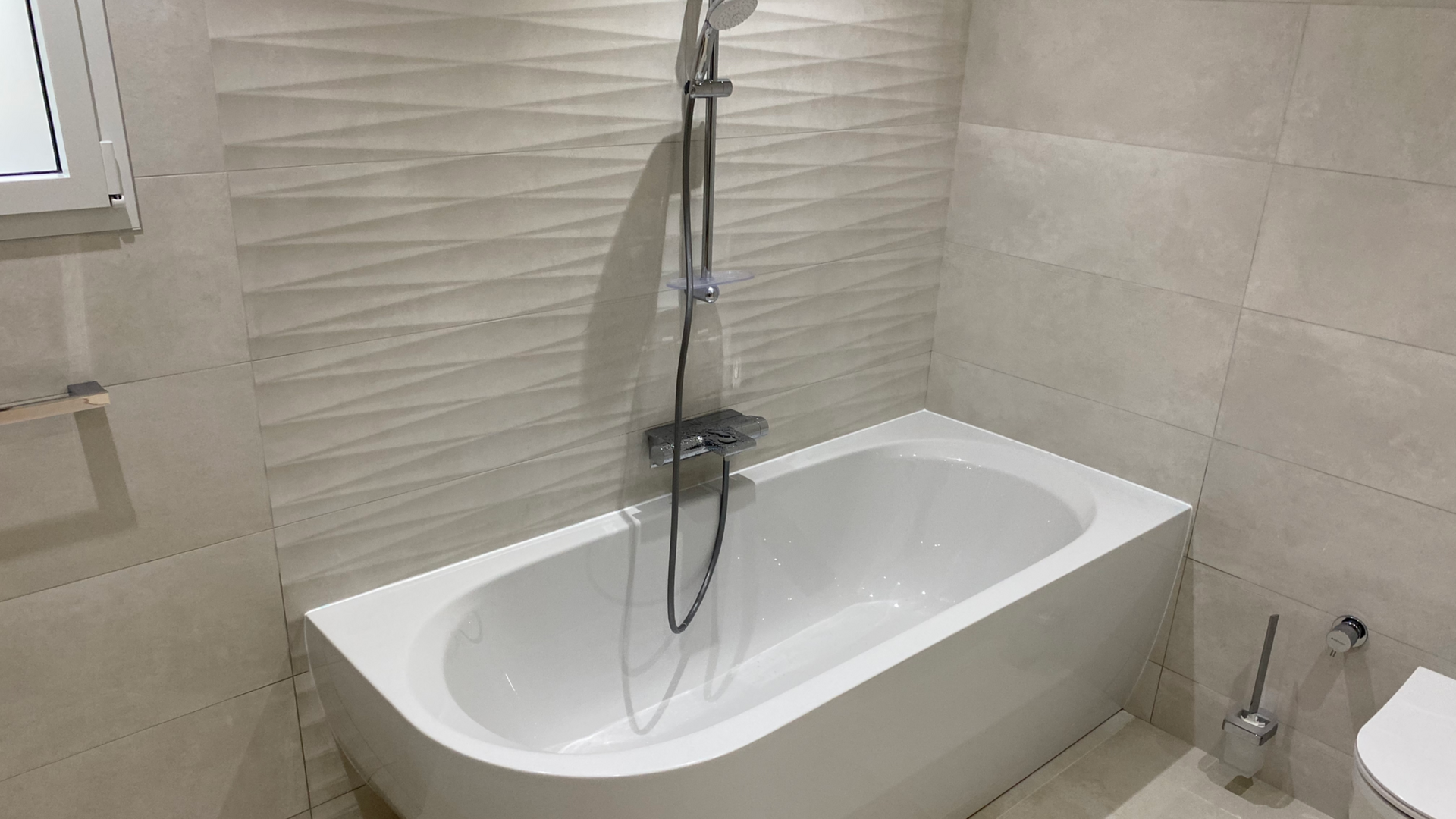 Baignoire blanche avec pommeau de douche et toilettes dans une salle de bains moderne.