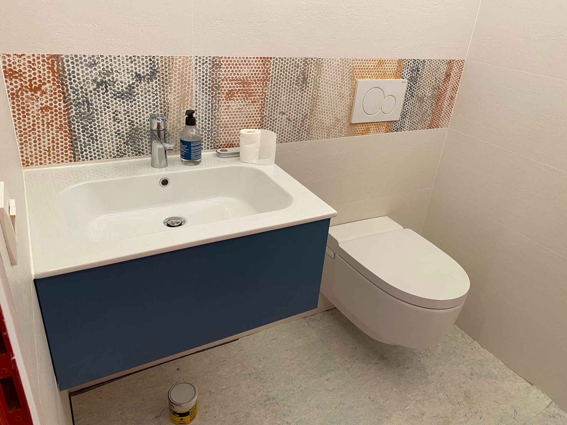 Petite salle de bains avec meuble-lavabo bleu, lavabo blanc et toilettes suspendues. Crédence en carrelage décoratif.