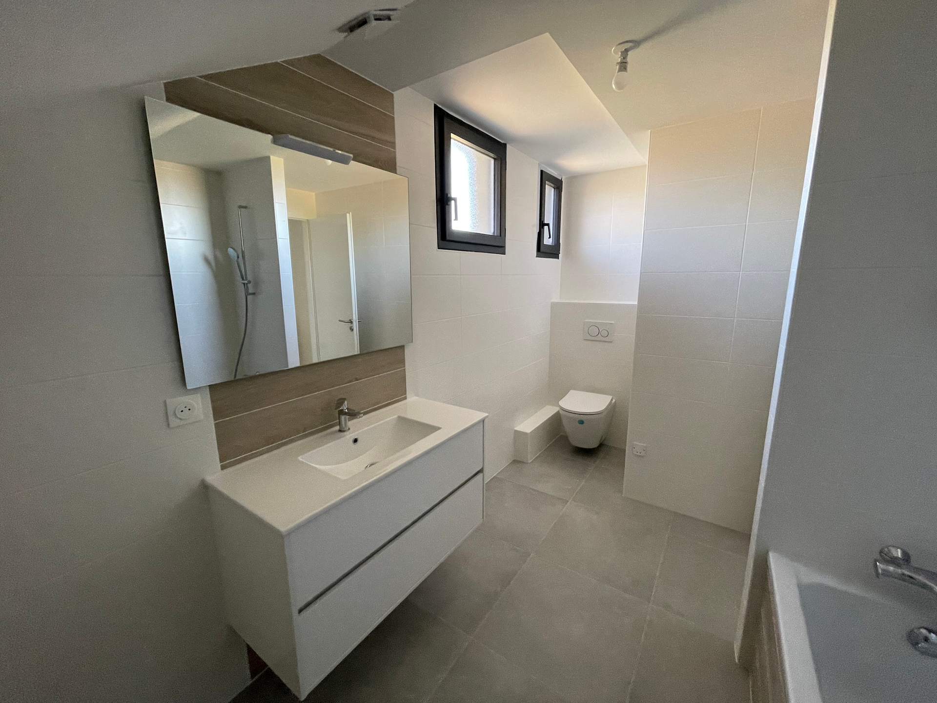 Salle de bains blanche moderne avec une vanité, des toilettes et un grand miroir.
