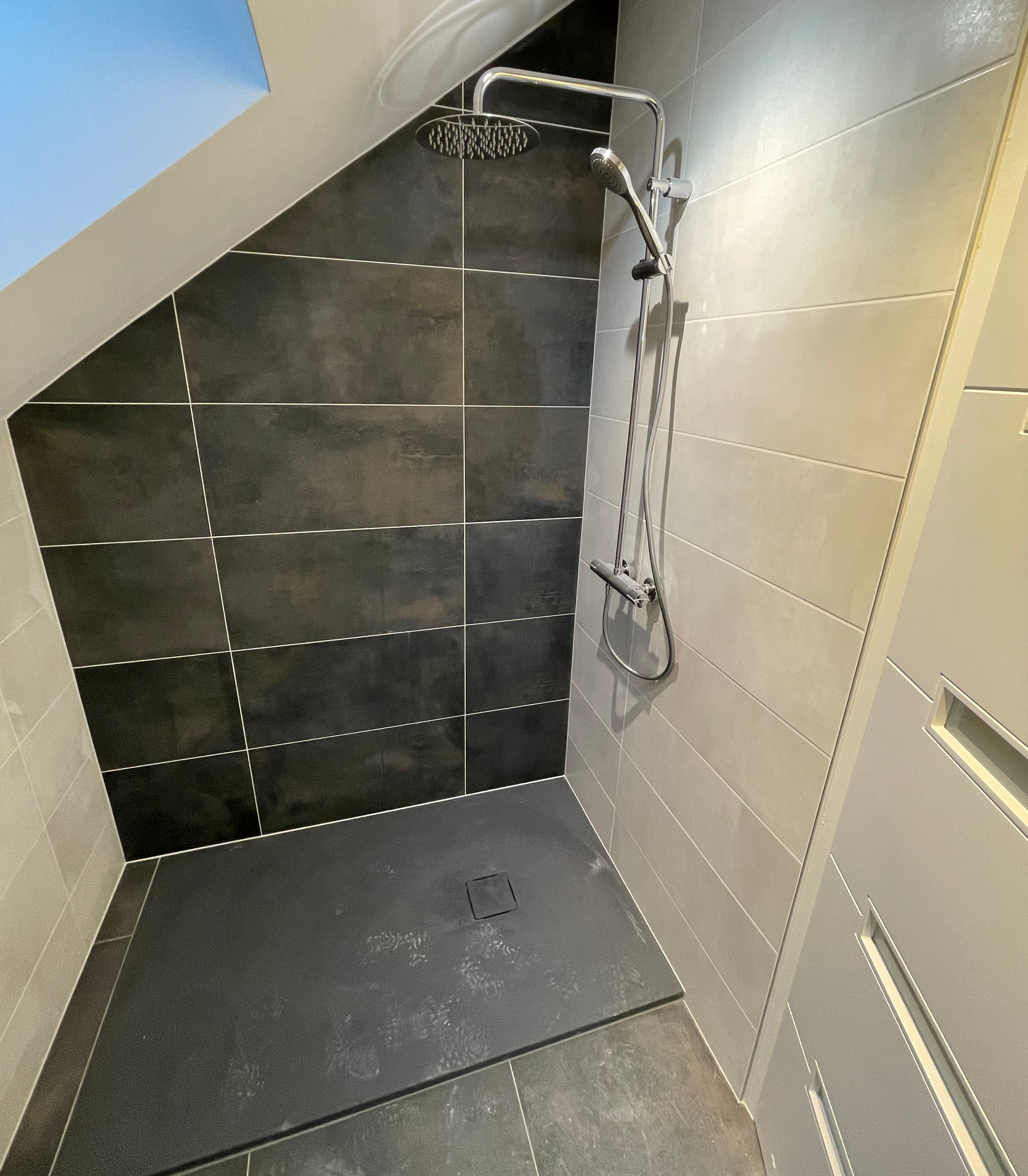 Une douche carrelée gris foncé avec une pomme de douche à effet pluie et un pulvérisateur à main dans une salle de bain moderne.