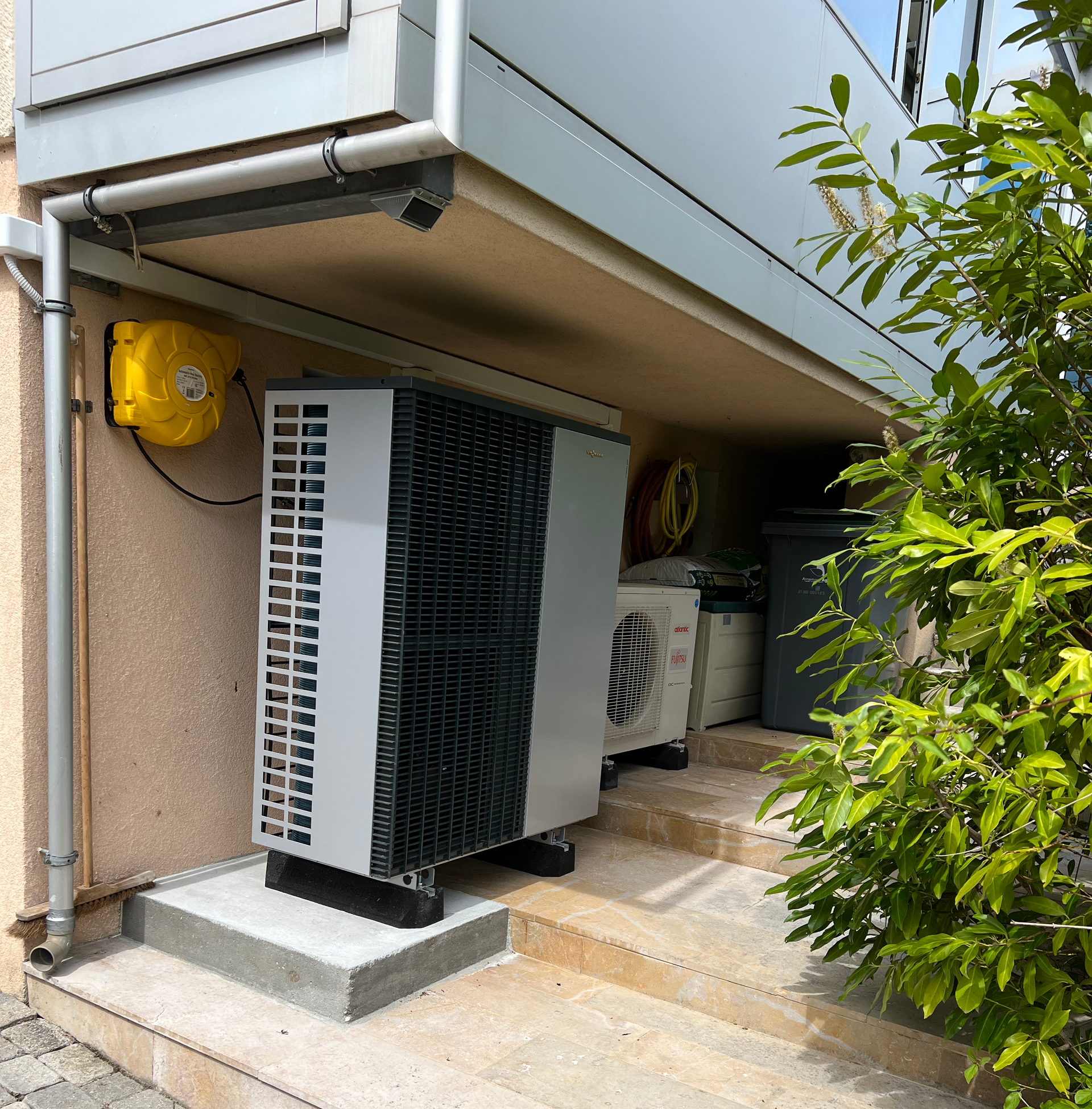 Unités de pompe à chaleur extérieures, argent et gris, près d'un bâtiment avec un boîtier électrique jaune.