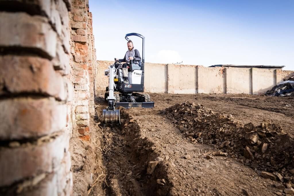 Un hombre conduce una pequeña excavadora en un campo de tierra.