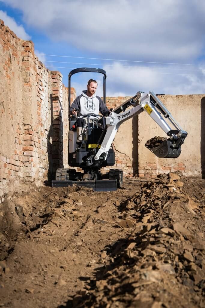 Un hombre conduce una pequeña excavadora en un campo de tierra.