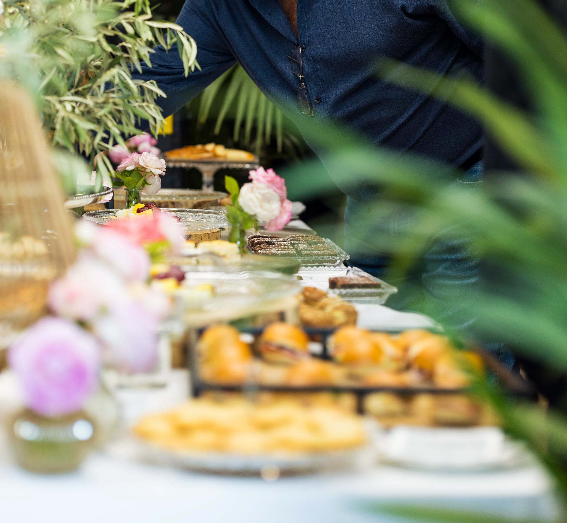 Une table garnie d'amuse-gueules et de pâtisseries lors d'un événement, avec des compositions florales.