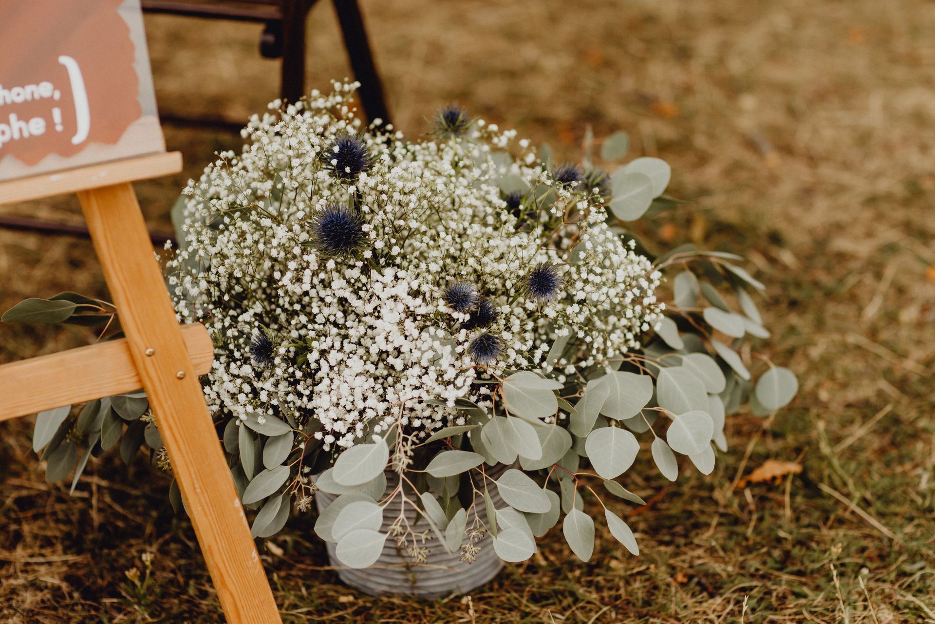 Un arrangement floral composé de gypsophile, de chardon bleu et de feuilles d'eucalyptus dans un panier, à côté d'un support en bois.