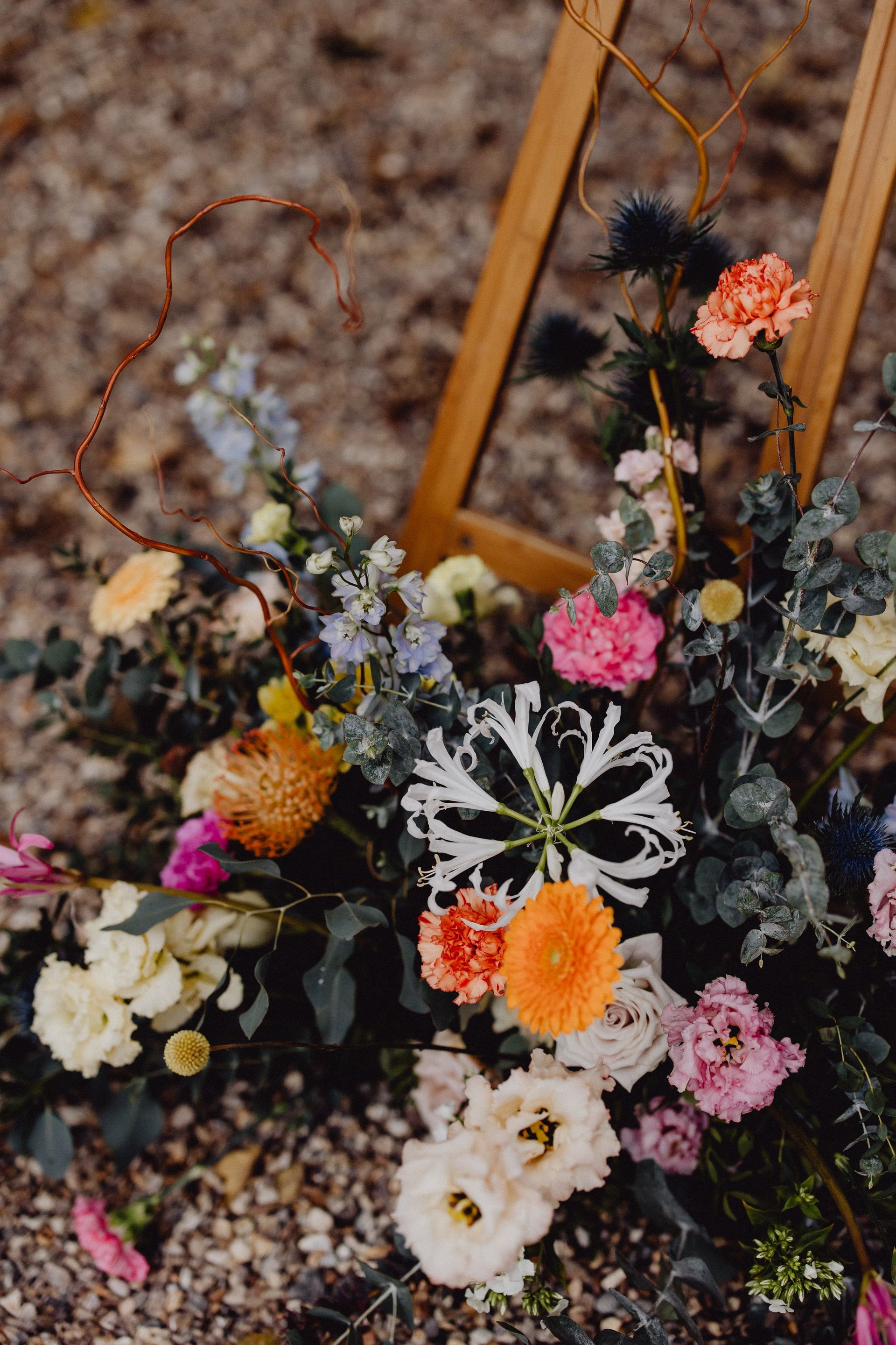 Une composition florale luxuriante et colorée, avec des fleurs orange, roses et blanches et du feuillage vert, placée près d'un cadre en bois.